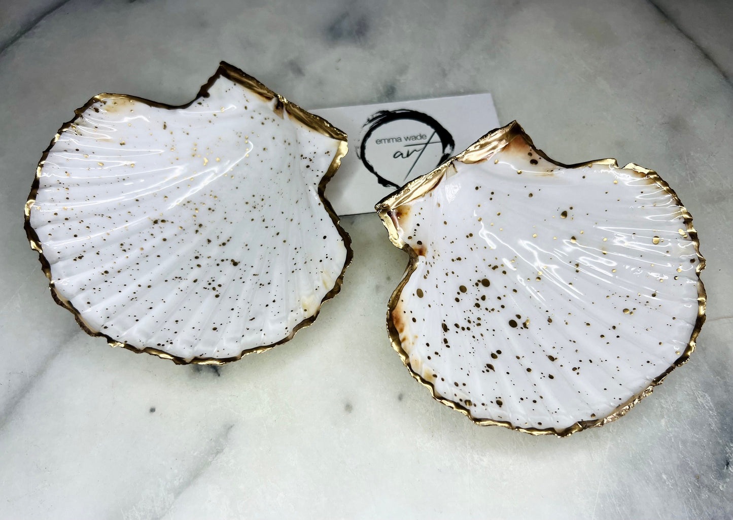 Handmade Dorset scallop shell trinket dishes featuring natural white shells with delicate liquid gold leaf speckling, hand-painted gold leaf edging and glossy crystal clear resin. Luxury coastal jewellery dishes styled on a white marble background with elegant neutral tones and artisan coastal home décor styling.