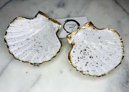Handmade Dorset scallop shell trinket dishes featuring natural white shells with delicate liquid gold leaf speckling, hand-painted gold leaf edging and glossy crystal clear resin. Luxury coastal jewellery dishes styled on a white marble background with elegant neutral tones and artisan coastal home décor styling.