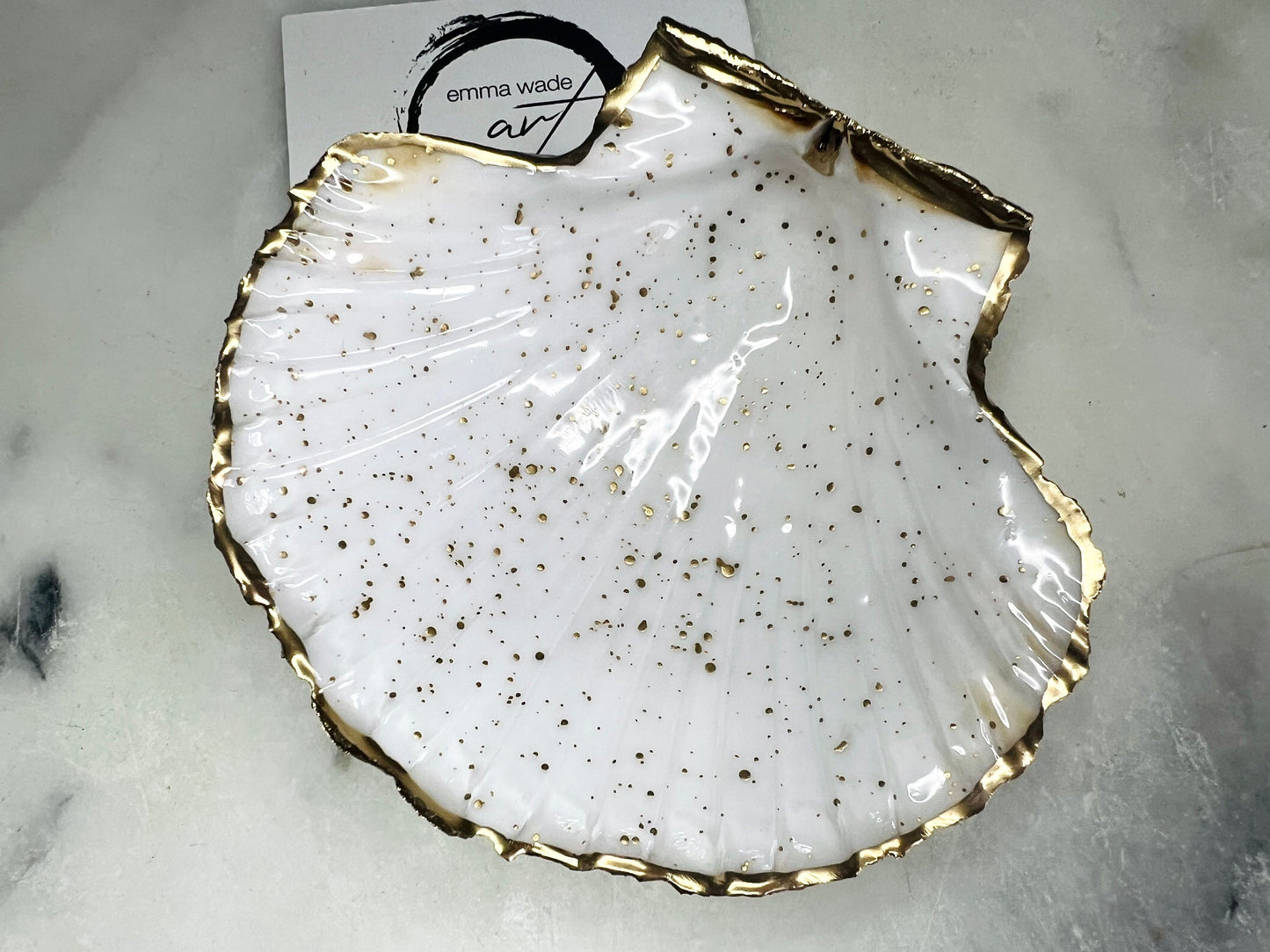 Handmade Dorset scallop shell trinket dishes featuring natural white shells with delicate liquid gold leaf speckling, hand-painted gold leaf edging and glossy crystal clear resin. Luxury coastal jewellery dishes styled on a white marble background with elegant neutral tones and artisan coastal home décor styling.
