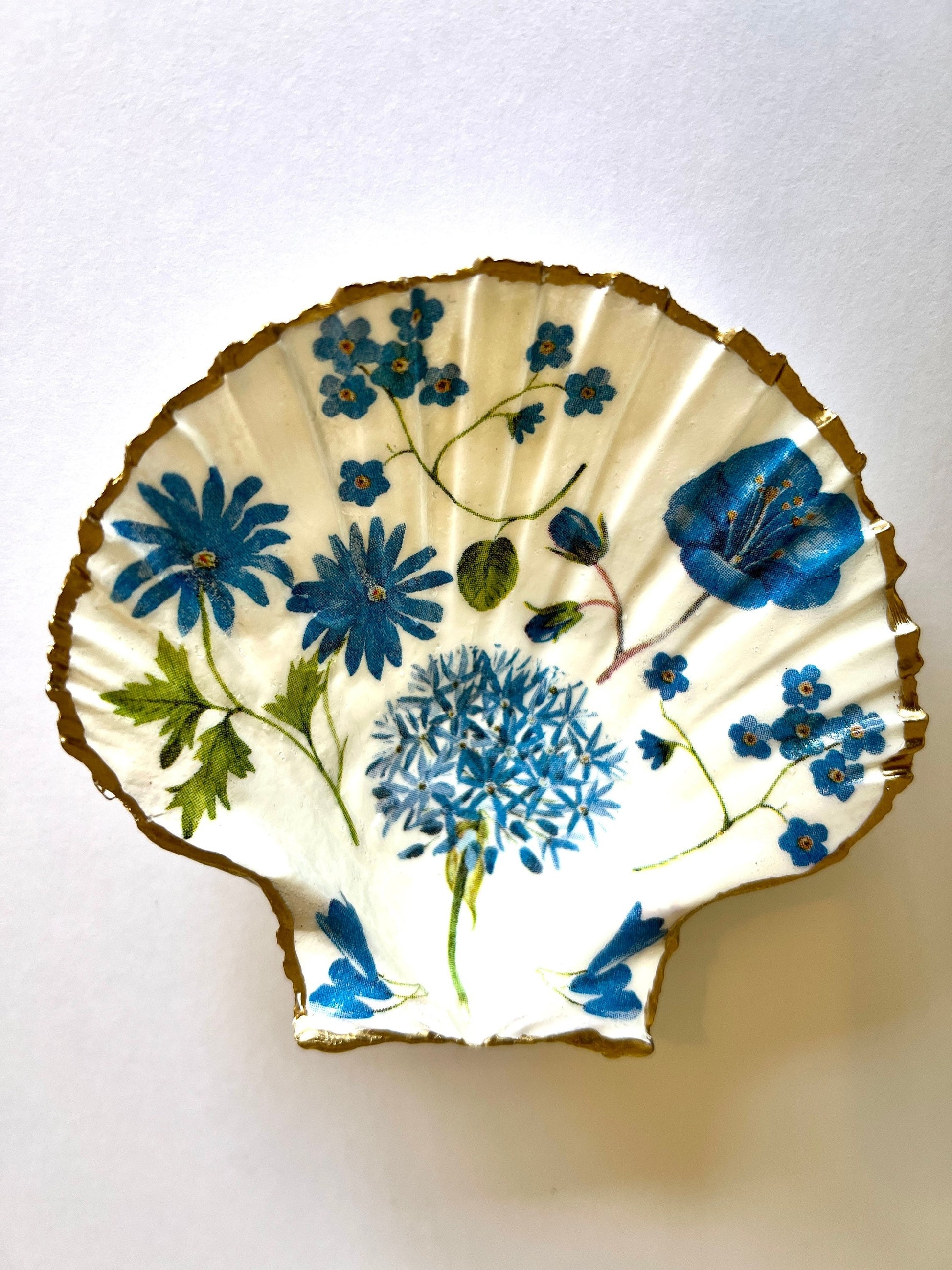 featuring delicate blue spring flowers including bluebells and forget-me-nots, finished with hand-applied gold leaf edging and glossy resin. Coastal shell ring holder and jewellery dish available in standard and large sizes, perfect for vanity décor, bridesmaid gifts, or elegant coastal home styling.