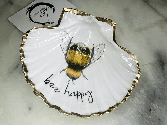 Handmade scallop shell trinket dish featuring a bumblebee illustration with gold leaf edging and glossy resin finish. Coastal jewellery dish in natural white shell with bee artwork, displayed as a ring holder and handmade bee lover gift