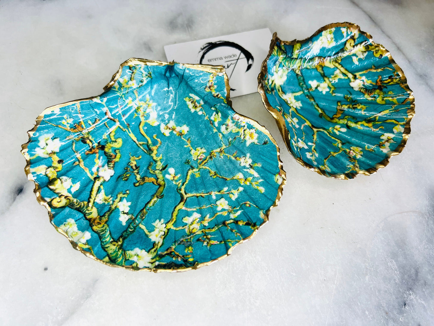 Handcrafted Dorset scallop shell trinket dish inspired by Vincent van Gogh’s Almond Blossom painting. Turquoise blue and green background with branching blossom design and raised gold detailing, finished with liquid gold leaf edging and sealed in high-gloss resin. Decorative shell jewellery holder styled on marble surface, suitable for rings, earrings, trinkets or as a tea light holder. Coastal art-inspired home decor piece.