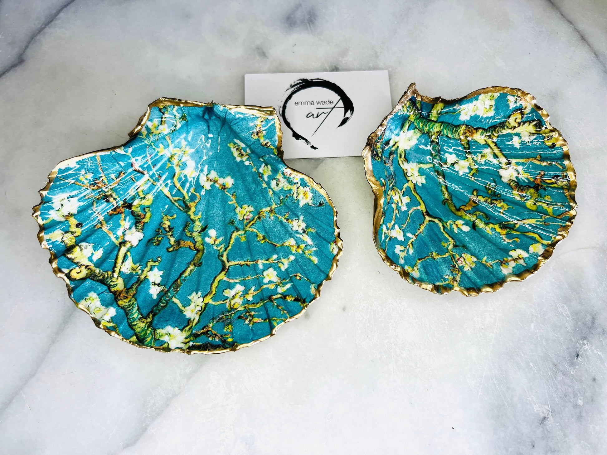 Handcrafted Dorset scallop shell trinket dish inspired by Vincent van Gogh’s Almond Blossom painting. Turquoise blue and green background with branching blossom design and raised gold detailing, finished with liquid gold leaf edging and sealed in high-gloss resin. Decorative shell jewellery holder styled on marble surface, suitable for rings, earrings, trinkets or as a tea light holder. Coastal art-inspired home decor piece.