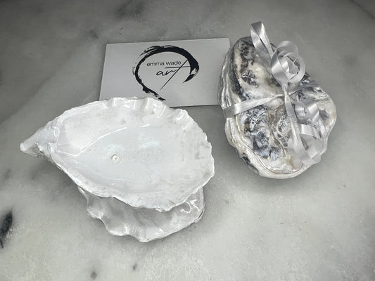 Handcrafted Dorset oyster shell ring box with matching natural shell lid, featuring a luminous inset Swarovski pearl nestled inside the cupped shell. Interior has a soft pearlescent white sheen and is sealed with crystal-clear resin. Optional outer finish in natural pearl tone or pearl with subtle gold leaf highlights. Coastal-inspired engagement proposal ring holder and wedding keepsake, styled on marble surface.