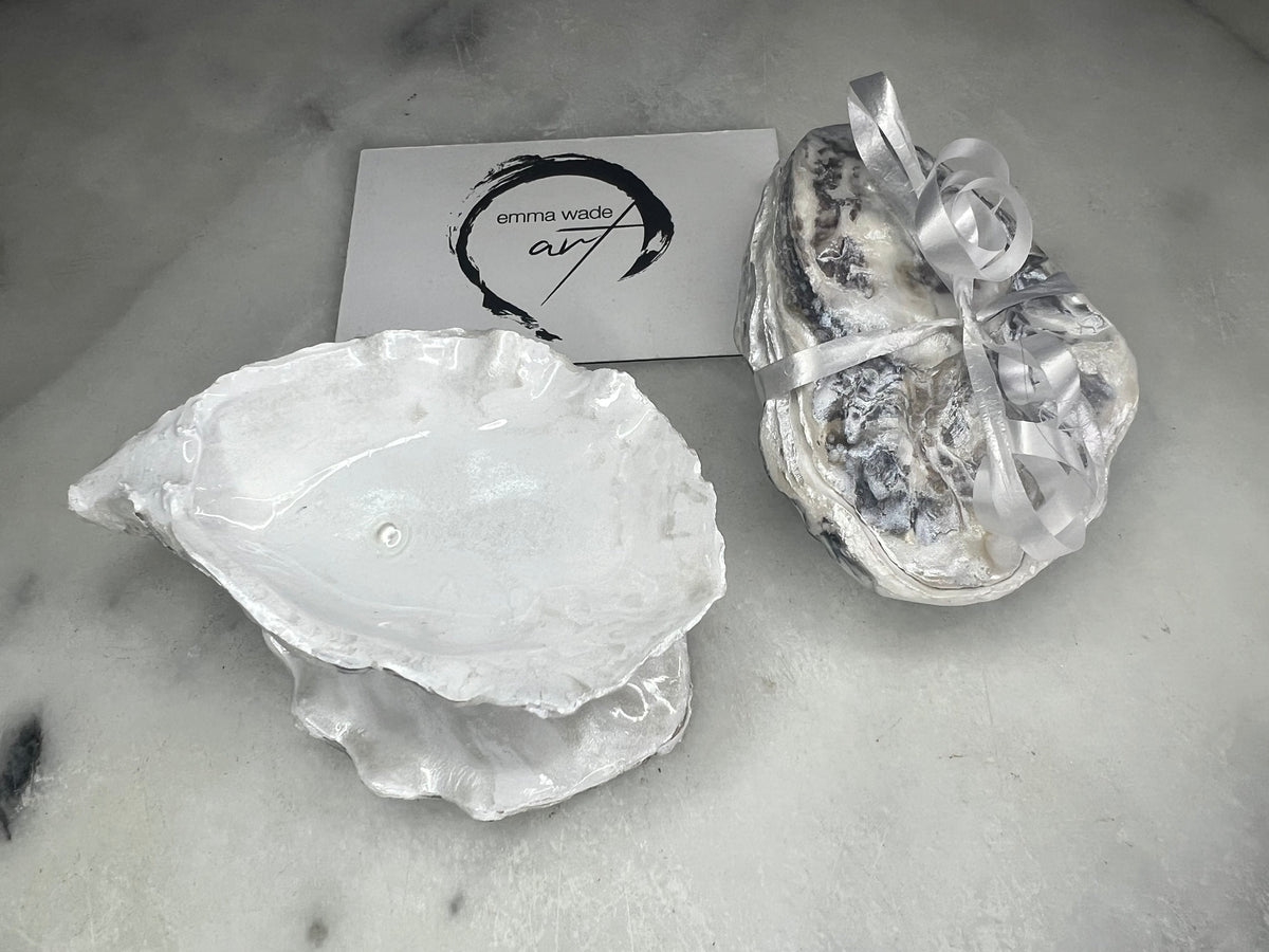 Handcrafted Dorset oyster shell ring box with matching natural shell lid, featuring a luminous inset Swarovski pearl nestled inside the cupped shell. Interior has a soft pearlescent white sheen and is sealed with crystal-clear resin. Optional outer finish in natural pearl tone or pearl with subtle gold leaf highlights. Coastal-inspired engagement proposal ring holder and wedding keepsake, styled on marble surface.