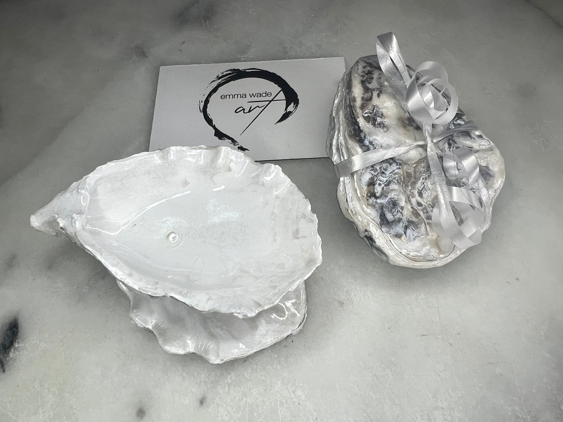 Handcrafted Dorset oyster shell ring box with matching natural shell lid, featuring a luminous inset Swarovski pearl nestled inside the cupped shell. Interior has a soft pearlescent white sheen and is sealed with crystal-clear resin. Optional outer finish in natural pearl tone or pearl with subtle gold leaf highlights. Coastal-inspired engagement proposal ring holder and wedding keepsake, styled on marble surface.