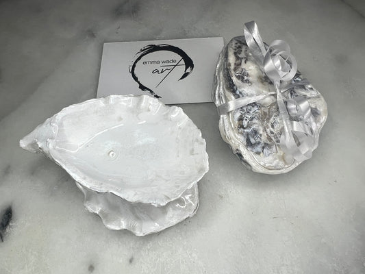 Handcrafted Dorset oyster shell ring box with matching natural shell lid, featuring a luminous inset Swarovski pearl nestled inside the cupped shell. Interior has a soft pearlescent white sheen and is sealed with crystal-clear resin. Optional outer finish in natural pearl tone or pearl with subtle gold leaf highlights. Coastal-inspired engagement proposal ring holder and wedding keepsake, styled on marble surface.