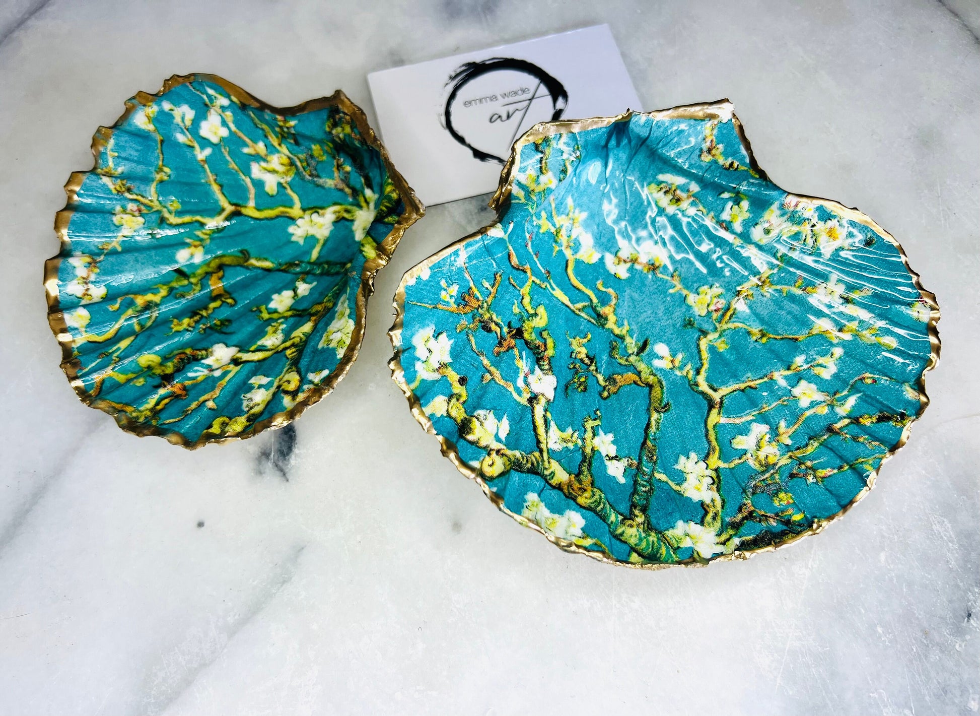 Handcrafted Dorset scallop shell trinket dish inspired by Vincent van Gogh’s Almond Blossom painting. Turquoise blue and green background with branching blossom design and raised gold detailing, finished with liquid gold leaf edging and sealed in high-gloss resin. Decorative shell jewellery holder styled on marble surface, suitable for rings, earrings, trinkets or as a tea light holder. Coastal art-inspired home decor piece.