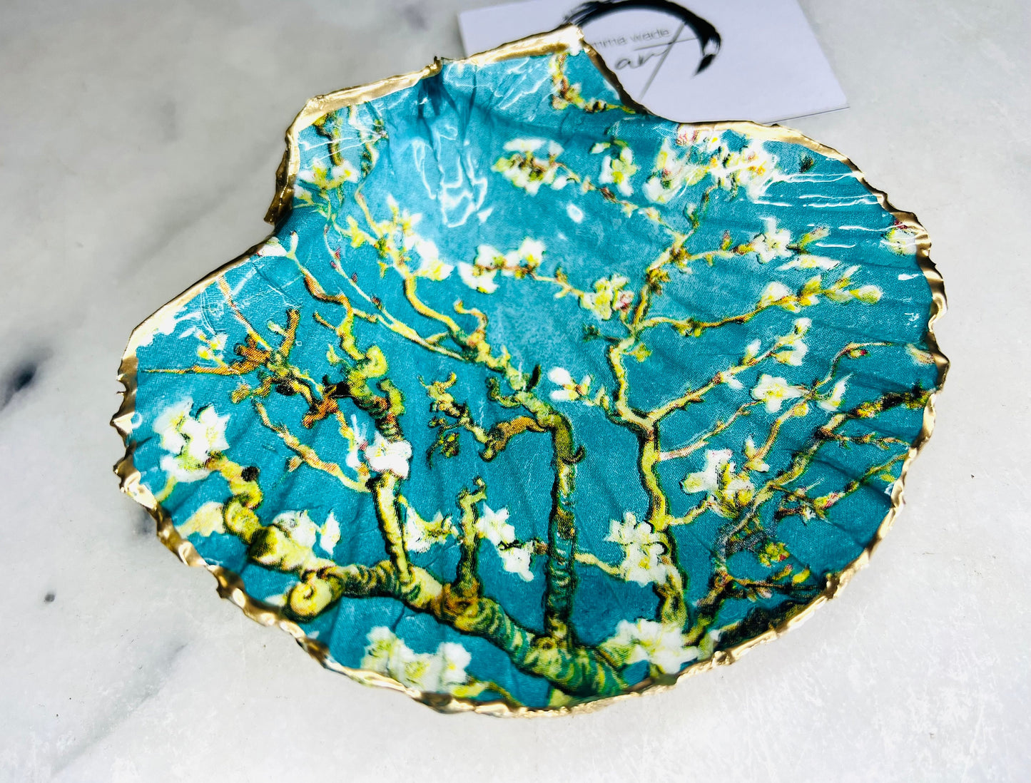 Handcrafted Dorset scallop shell trinket dish inspired by Vincent van Gogh’s Almond Blossom painting. Turquoise blue and green background with branching blossom design and raised gold detailing, finished with liquid gold leaf edging and sealed in high-gloss resin. Decorative shell jewellery holder styled on marble surface, suitable for rings, earrings, trinkets or as a tea light holder. Coastal art-inspired home decor piece.