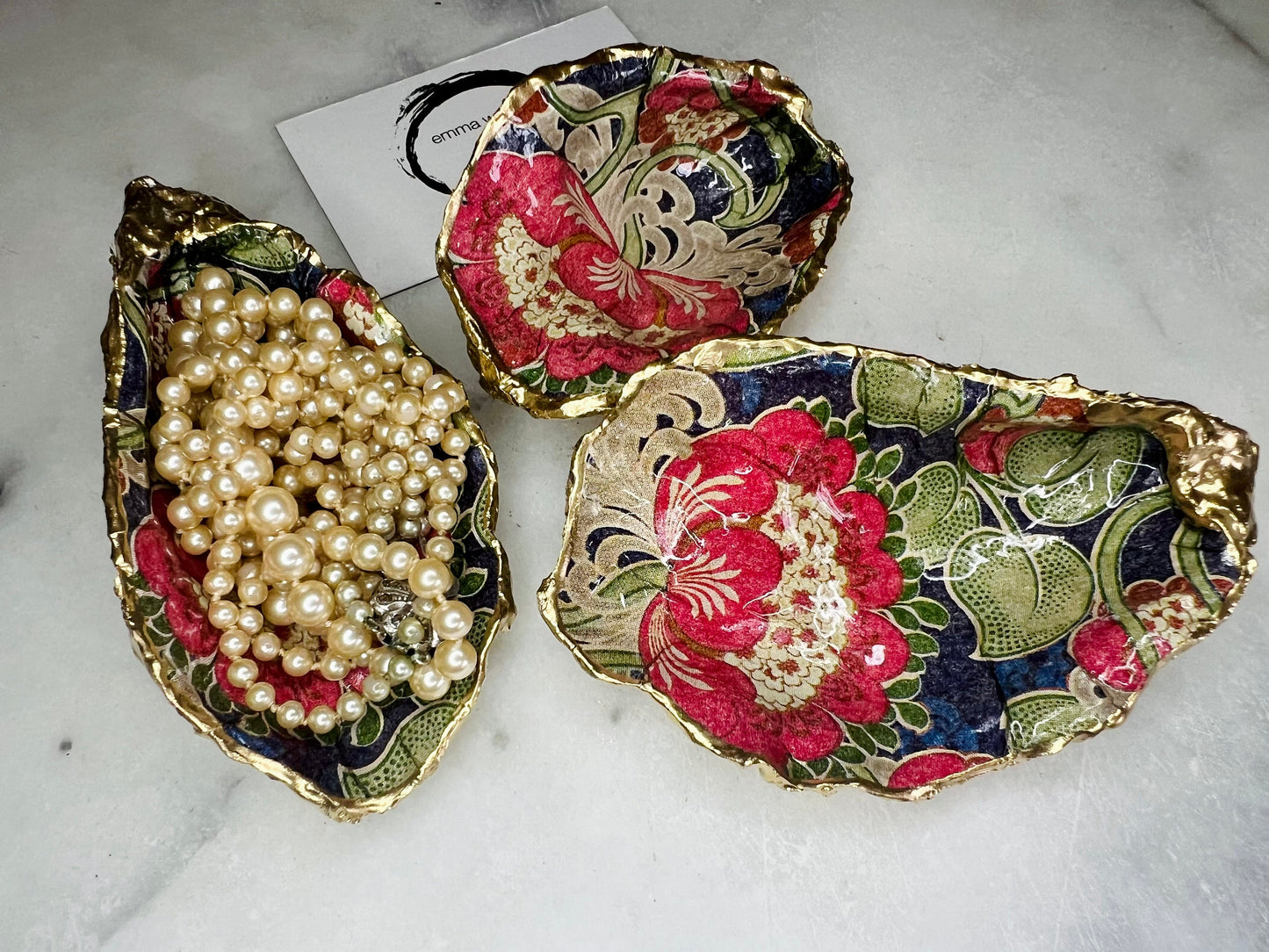 Handmade oyster shell trinket dish featuring a retro floral botanical pattern in pink, red, navy, and olive tones with gold leaf edging and glossy resin finish. Vintage V&A inspired oyster shell jewellery dish styled as coastal cottagecore home décor.