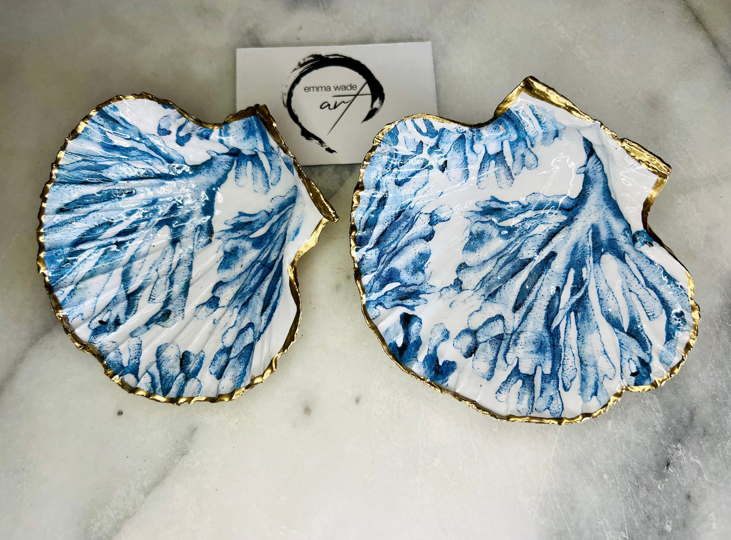 Blue seaweed scallop shell ring catcher with hand applied gold leaf edging and glossy resin finish. Handmade Dorset shell jewellery tray with ocean inspired design styled on marble background. Coastal vanity decor and beach house accessory with optional gold driftwood stand.