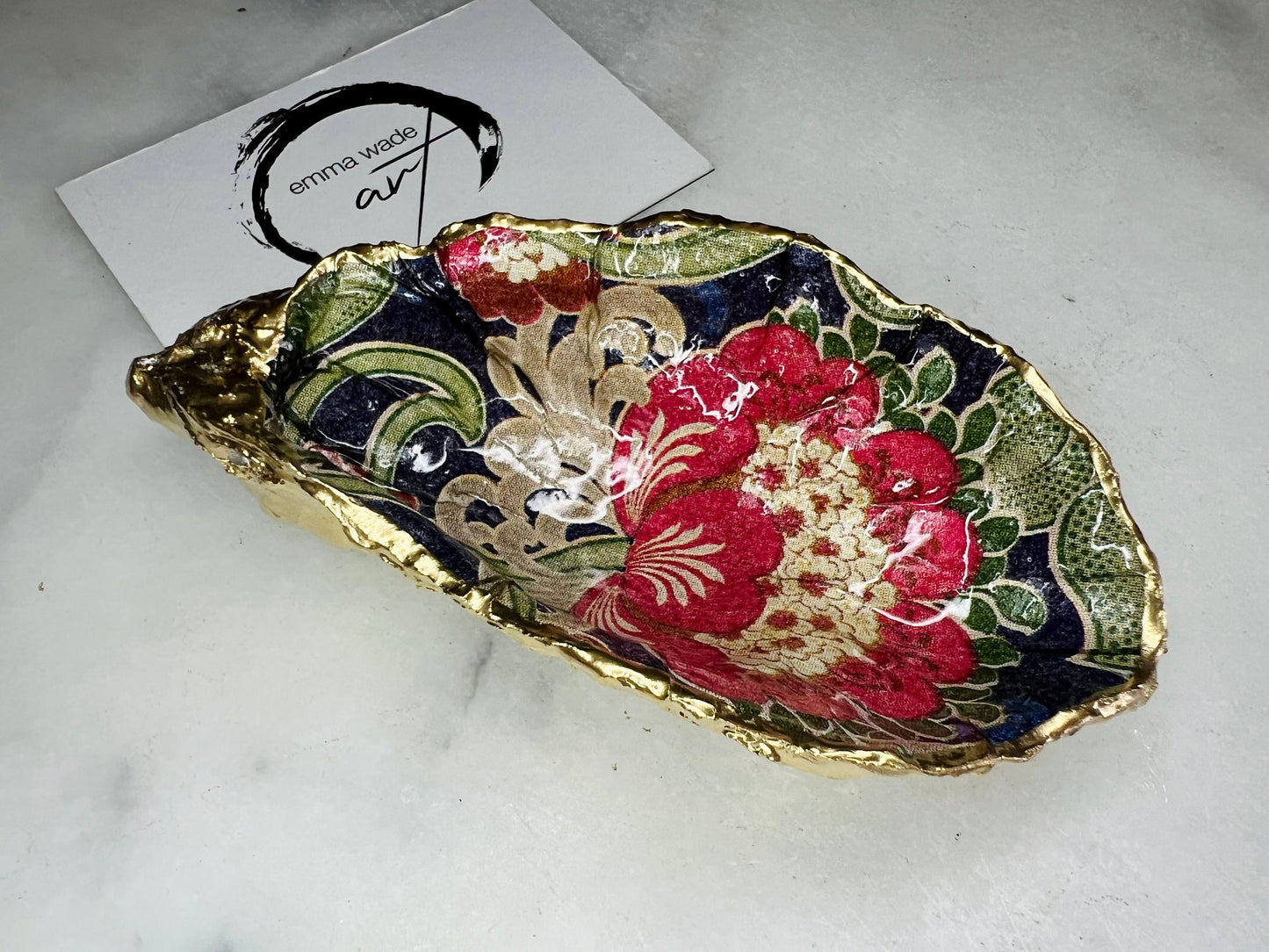 Handmade oyster shell trinket dish featuring a retro floral botanical pattern in pink, red, navy, and olive tones with gold leaf edging and glossy resin finish. Vintage V&A inspired oyster shell jewellery dish styled as coastal cottagecore home décor.