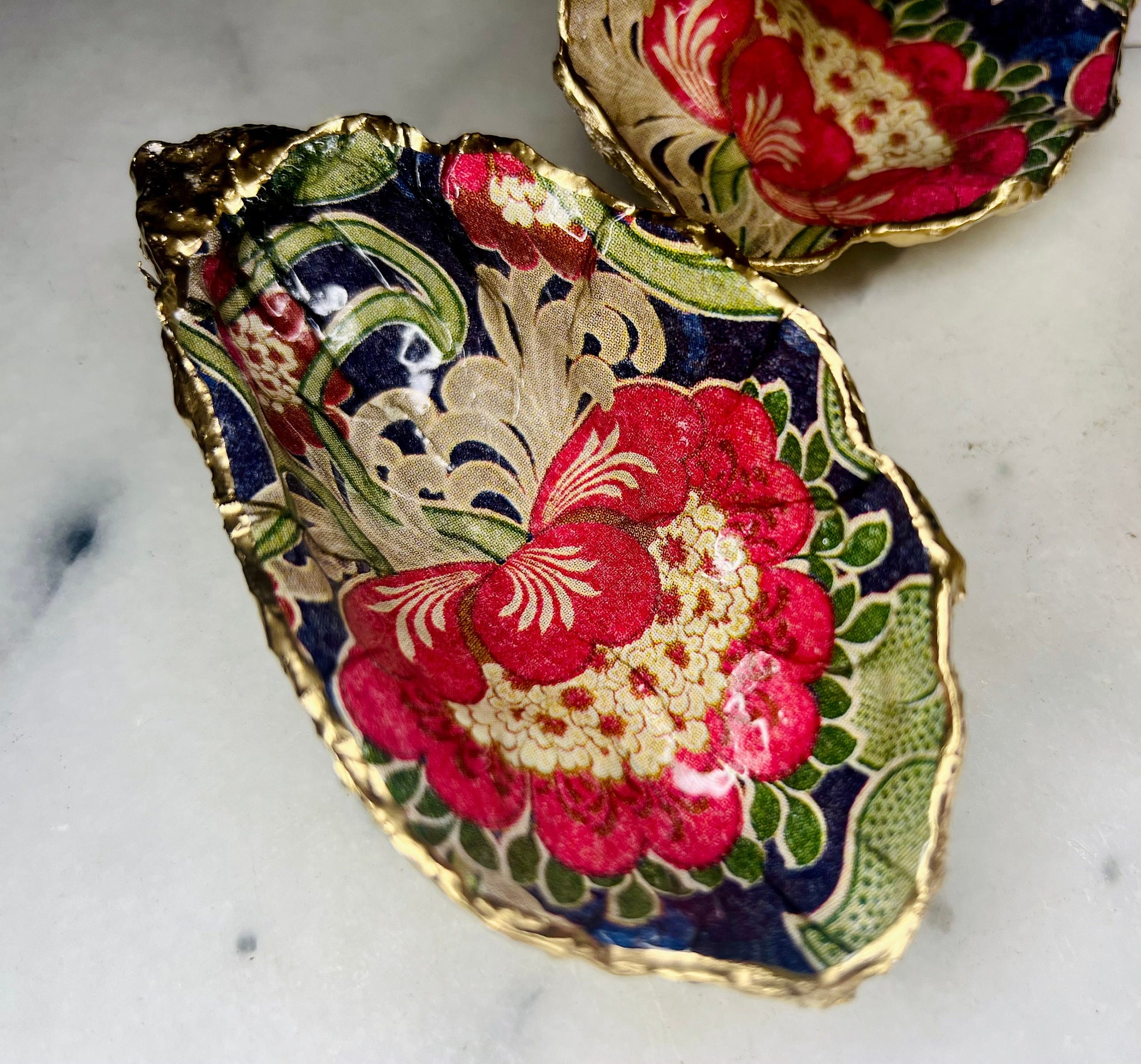 Handmade oyster shell trinket dish featuring a retro floral botanical pattern in pink, red, navy, and olive tones with gold leaf edging and glossy resin finish. Vintage V&A inspired oyster shell jewellery dish styled as coastal cottagecore home décor.