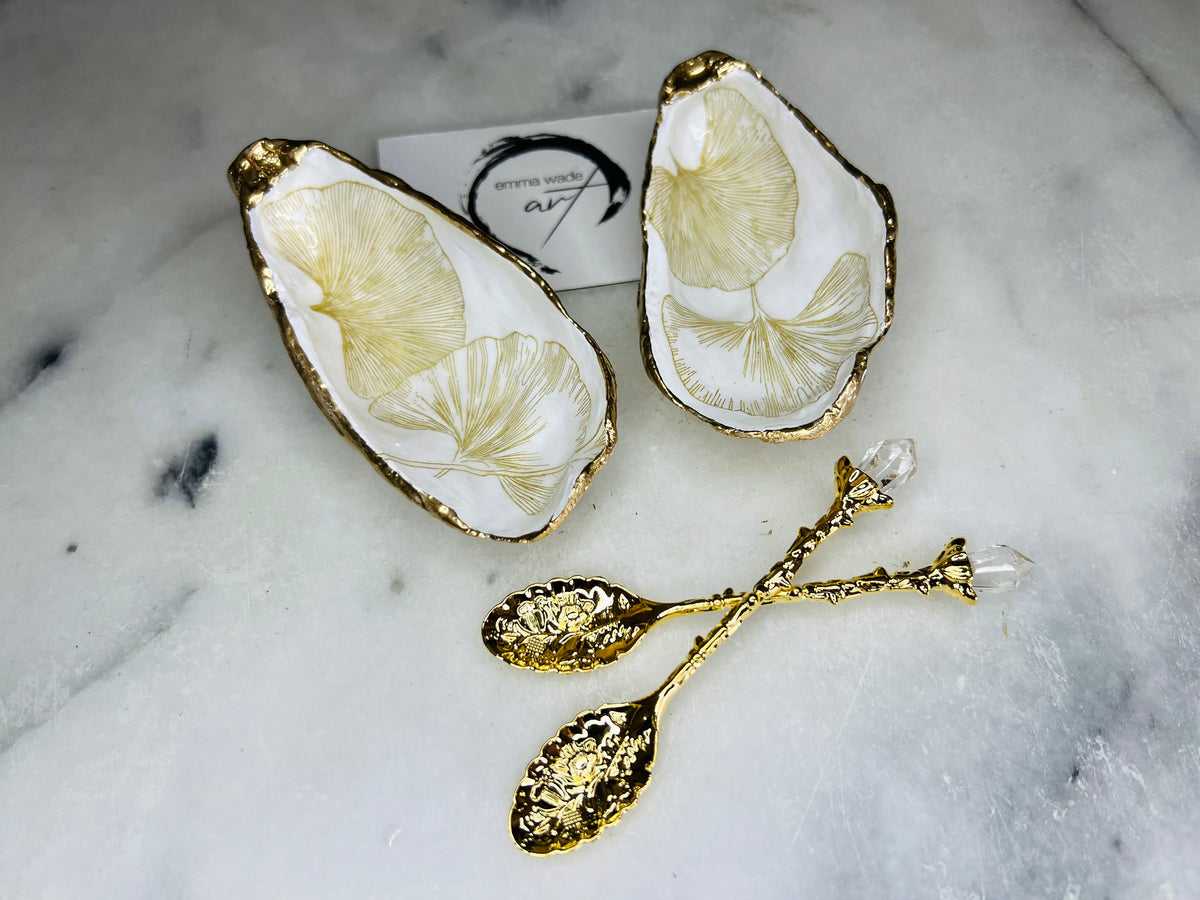 Pair of handmade Dorset oyster shell salt and pepper pinch pots featuring elegant Japanese Ginkgo floral artwork in soft gold and pearl tones with hand-applied gold leaf edging. Coastal luxury cruet set sealed in glossy Crystal resin with optional gold crystal spoons.