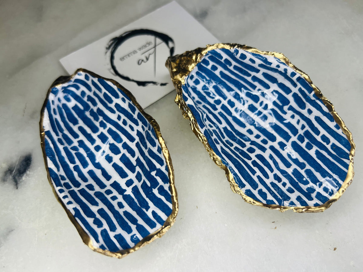 Pair of handmade blue and white lined oyster shell salt and pepper pinch pots with gold leaf trim, shown on a light background with small gold spoons. Crafted from natural Dorset oyster shells and sealed with glossy, food-safe resin, these coastal-inspired shell dishes are designed for table styling, weddings, or a unique hostess gift. Each shell is one of a kind and finished by hand.