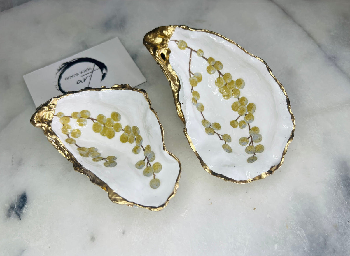 Pair of white and gold oyster shell salt and pepper pinch pots with delicate berry botanical design, hand gilded gold leaf edging and glossy resin finish. Handmade Dorset coastal shell dishes styled with gold crystal spoons on a marble background.