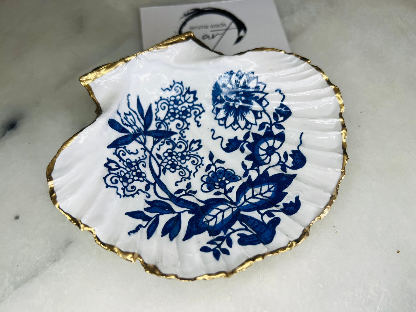 Handmade blue onion floral scallop shell trinket dish with gold leaf edging, shown on a light background. Crafted from a natural Dorset scallop shell, the dish features a classic blue and white floral pattern inspired by traditional onion designs, sealed with glossy epoxy resin. Designed as a jewellery or ring holder, this decorative shell dish is finished by hand and each piece is unique.