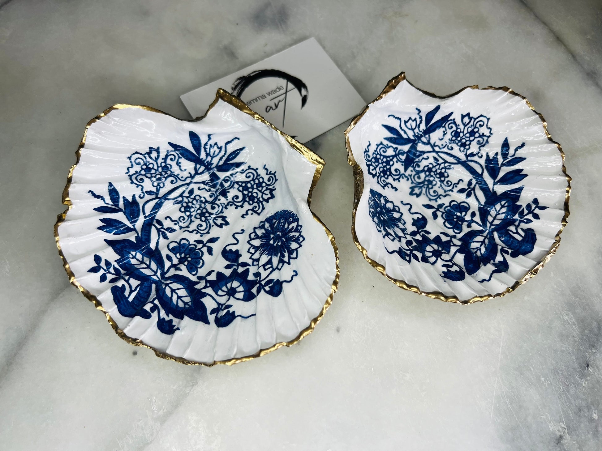 Handmade blue onion floral scallop shell trinket dish with gold leaf edging, shown on a light background. Crafted from a natural Dorset scallop shell, the dish features a classic blue and white floral pattern inspired by traditional onion designs, sealed with glossy epoxy resin. Designed as a jewellery or ring holder, this decorative shell dish is finished by hand and each piece is unique.