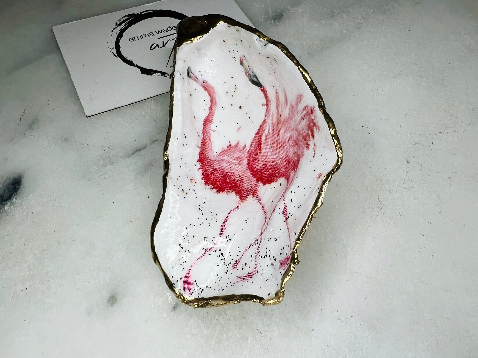 Handmade Dorset oyster shell trinket dishes featuring elegant pink flamingo bird artwork with hand-painted gold leaf edging and glossy crystal clear resin. Coastal flamingo jewellery holders styled on a white marble background with tropical blush pink tones and luxury coastal home décor styling.