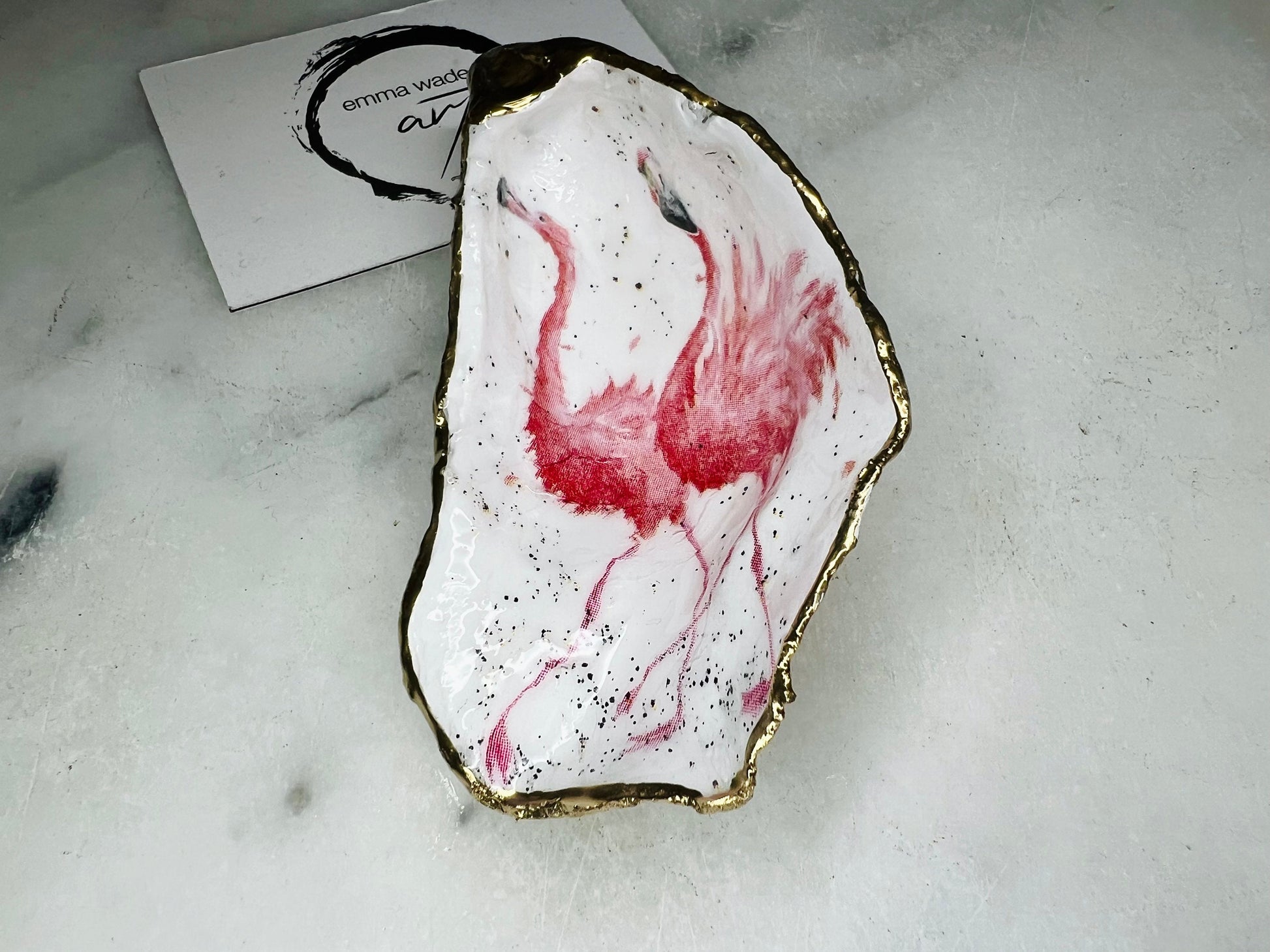 Handmade Dorset oyster shell trinket dishes featuring elegant pink flamingo bird artwork with hand-painted gold leaf edging and glossy crystal clear resin. Coastal flamingo jewellery holders styled on a white marble background with tropical blush pink tones and luxury coastal home décor styling.