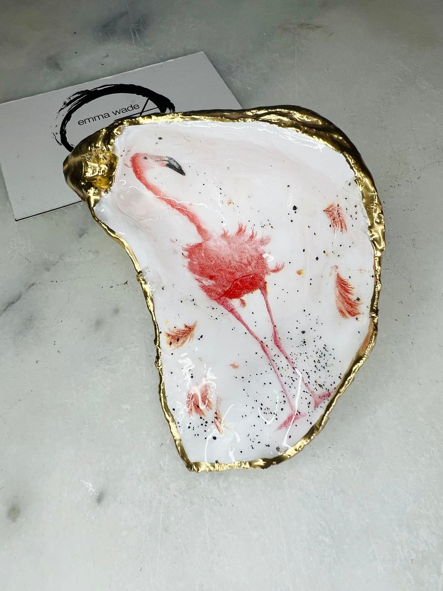 Handmade Dorset oyster shell trinket dishes featuring elegant pink flamingo bird artwork with hand-painted gold leaf edging and glossy crystal clear resin. Coastal flamingo jewellery holders styled on a white marble background with tropical blush pink tones and luxury coastal home décor styling.