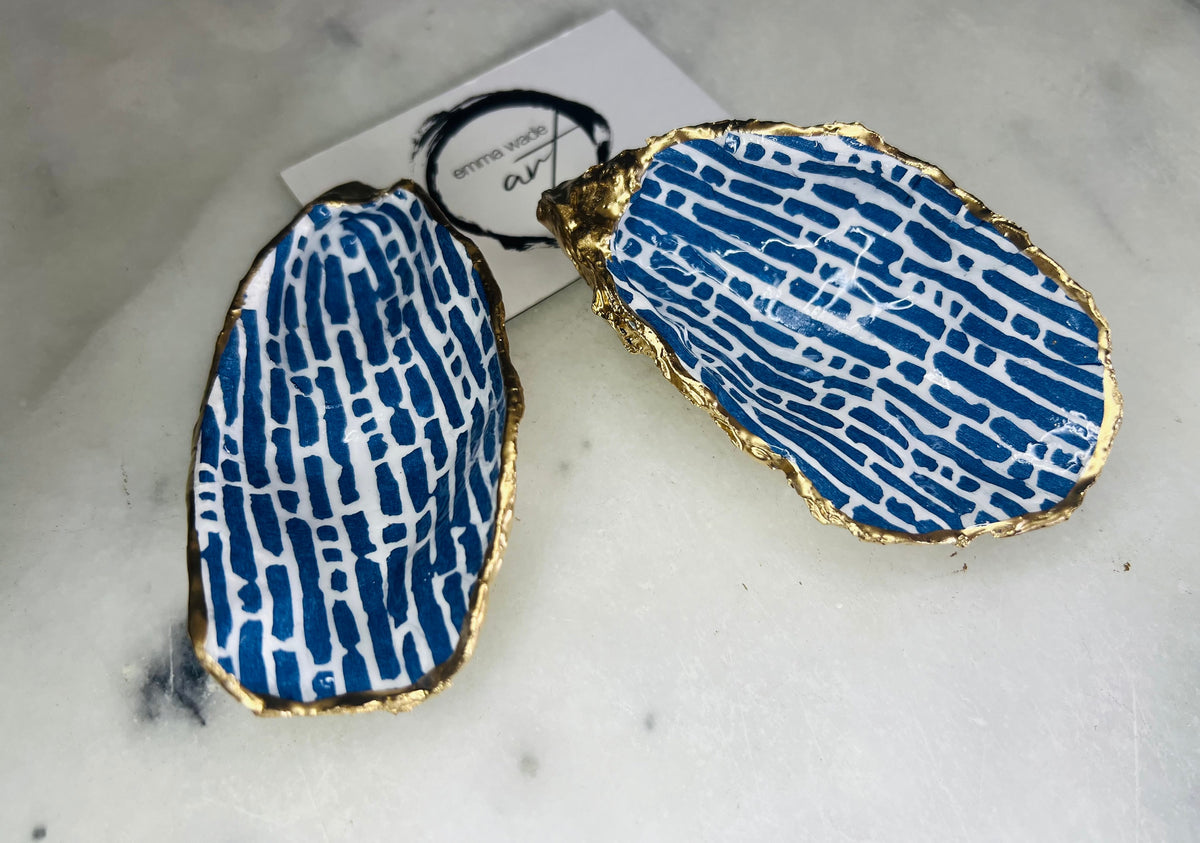 Pair of handmade blue and white lined oyster shell salt and pepper pinch pots with gold leaf trim, shown on a light background with small gold spoons. Crafted from natural Dorset oyster shells and sealed with glossy, food-safe resin, these coastal-inspired shell dishes are designed for table styling, weddings, or a unique hostess gift. Each shell is one of a kind and finished by hand.