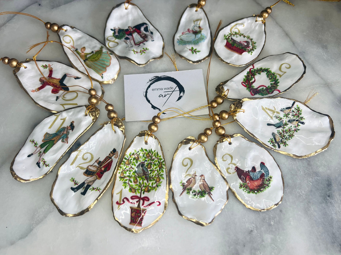 Handmade Twelve Days of Christmas oyster shell ornament set featuring all twelve traditional carol illustrations, finished with gold leaf edging, glossy resin and gold hanging cords. Coastal heirloom Christmas decorations handcrafted from Dorset oyster shells.