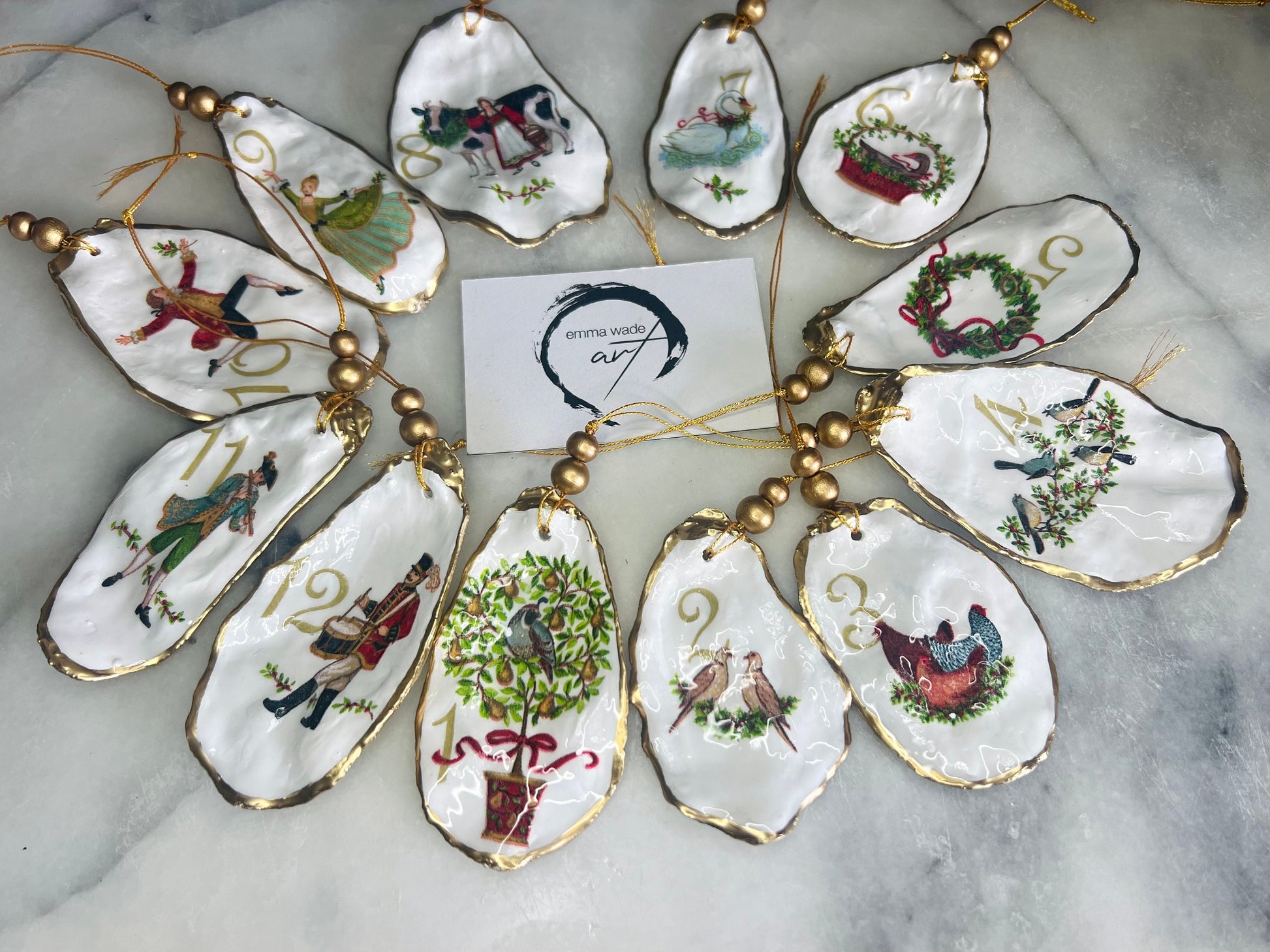 Handmade Twelve Days of Christmas oyster shell ornament set featuring all twelve traditional carol illustrations, finished with gold leaf edging, glossy resin and gold hanging cords. Coastal heirloom Christmas decorations handcrafted from Dorset oyster shells.