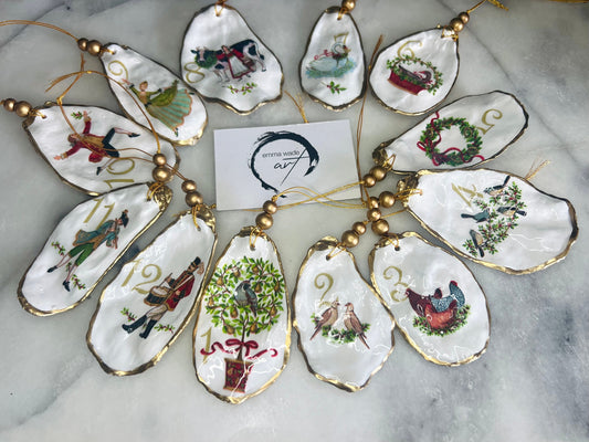 Handmade Twelve Days of Christmas oyster shell ornament set featuring all twelve traditional carol illustrations, finished with gold leaf edging, glossy resin and gold hanging cords. Coastal heirloom Christmas decorations handcrafted from Dorset oyster shells.