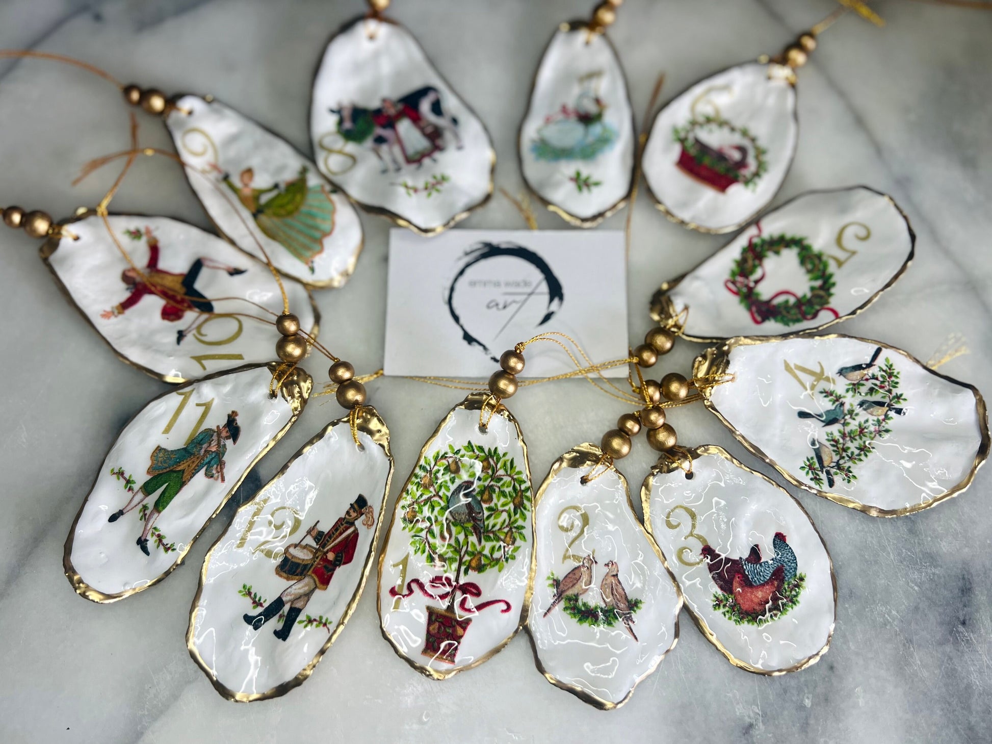 Handmade Twelve Days of Christmas oyster shell ornament set featuring all twelve traditional carol illustrations, finished with gold leaf edging, glossy resin and gold hanging cords. Coastal heirloom Christmas decorations handcrafted from Dorset oyster shells.