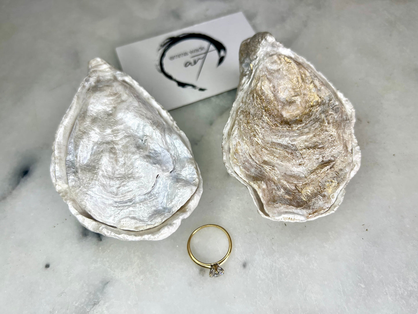 Handcrafted Dorset oyster shell ring box with matching natural shell lid, featuring a luminous inset Swarovski pearl nestled inside the cupped shell. Interior has a soft pearlescent white sheen and is sealed with crystal-clear resin. Optional outer finish in natural pearl tone or pearl with subtle gold leaf highlights. Coastal-inspired engagement proposal ring holder and wedding keepsake, styled on marble surface.
