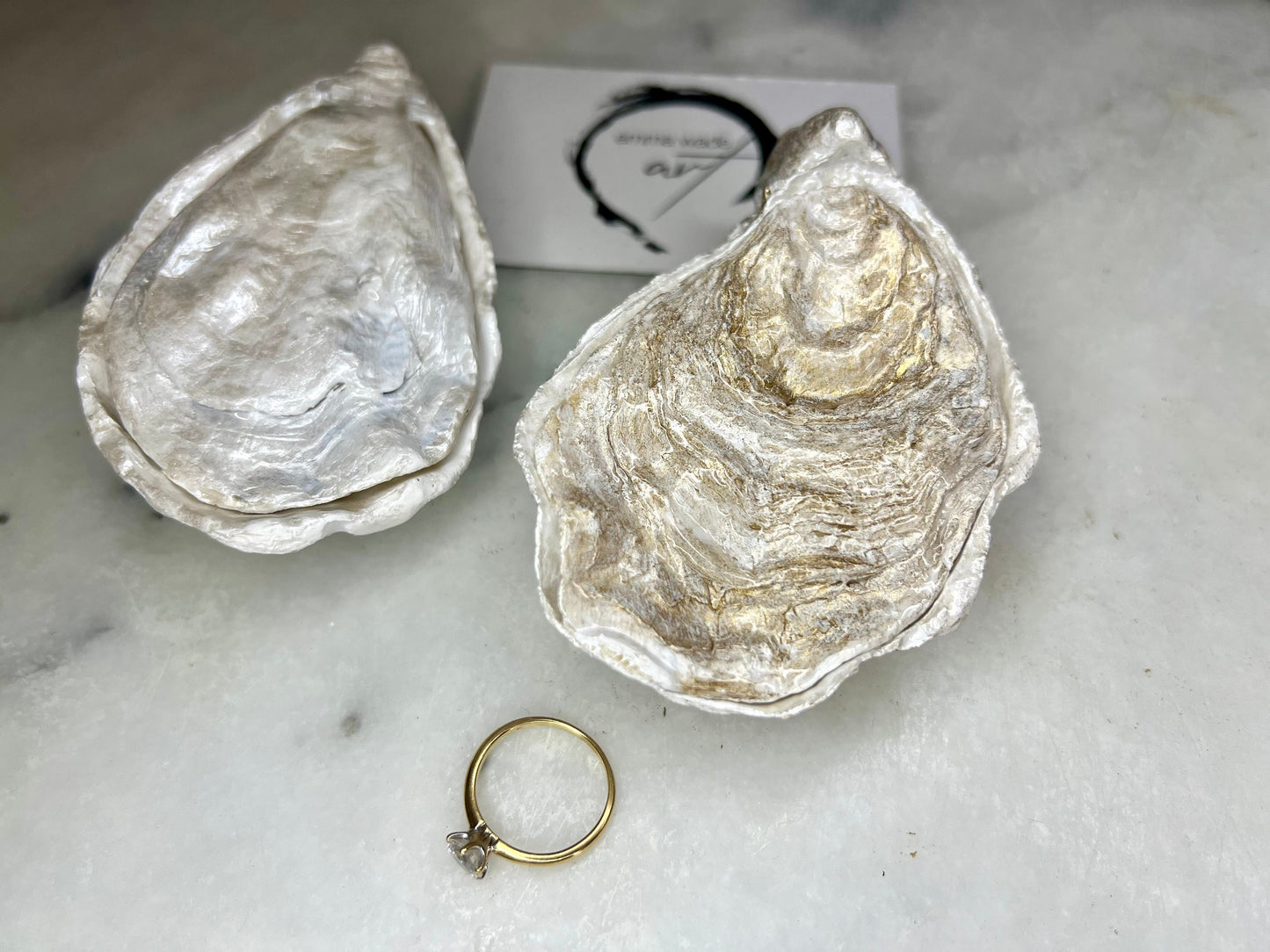 Handcrafted Dorset oyster shell ring box with matching natural shell lid, featuring a luminous inset Swarovski pearl nestled inside the cupped shell. Interior has a soft pearlescent white sheen and is sealed with crystal-clear resin. Optional outer finish in natural pearl tone or pearl with subtle gold leaf highlights. Coastal-inspired engagement proposal ring holder and wedding keepsake, styled on marble surface.