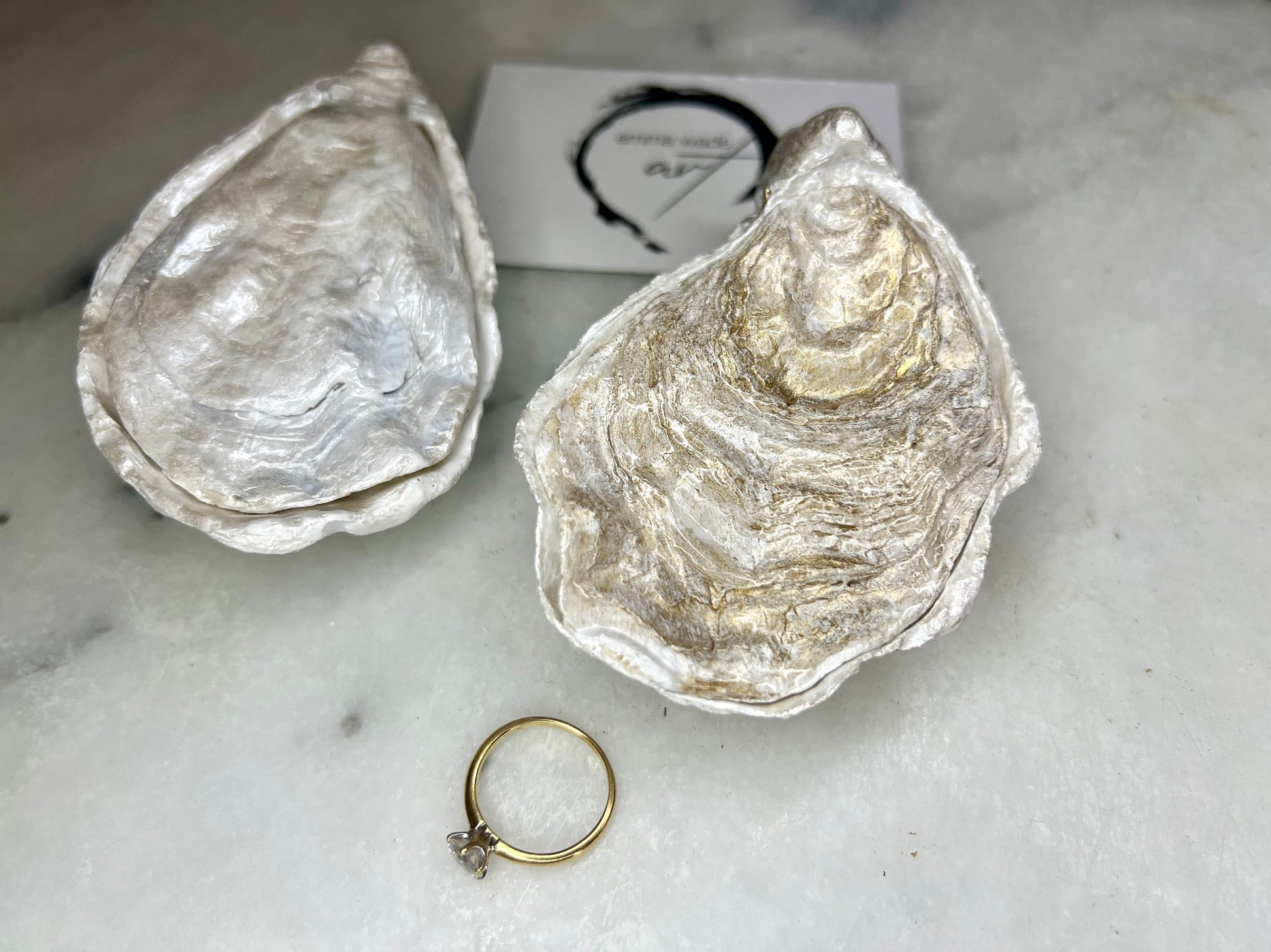 Handcrafted Dorset oyster shell ring box with matching natural shell lid, featuring a luminous inset Swarovski pearl nestled inside the cupped shell. Interior has a soft pearlescent white sheen and is sealed with crystal-clear resin. Optional outer finish in natural pearl tone or pearl with subtle gold leaf highlights. Coastal-inspired engagement proposal ring holder and wedding keepsake, styled on marble surface.
