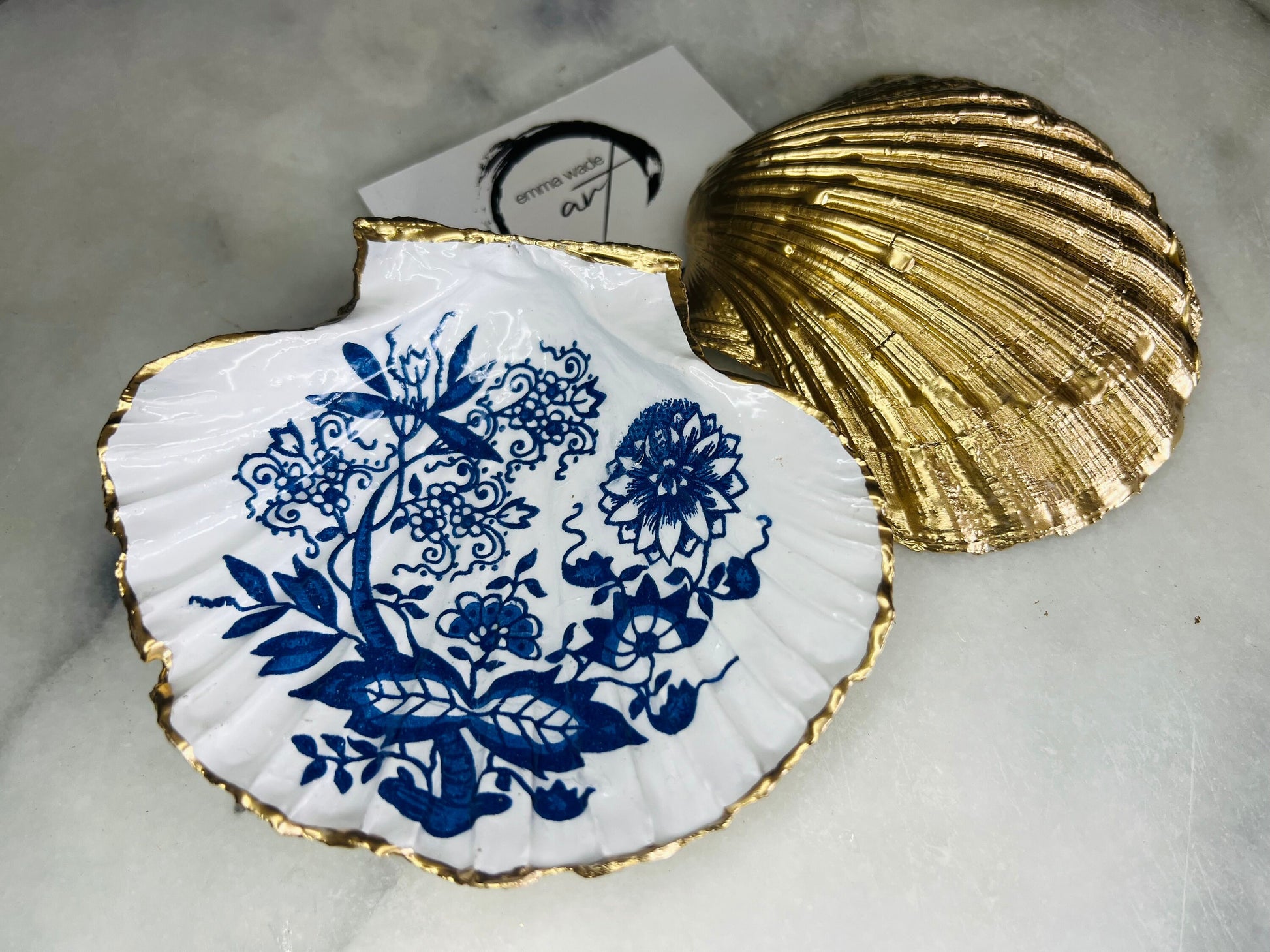 Handmade blue onion floral scallop shell trinket dish with gold leaf edging, shown on a light background. Crafted from a natural Dorset scallop shell, the dish features a classic blue and white floral pattern inspired by traditional onion designs, sealed with glossy epoxy resin. Designed as a jewellery or ring holder, this decorative shell dish is finished by hand and each piece is unique.