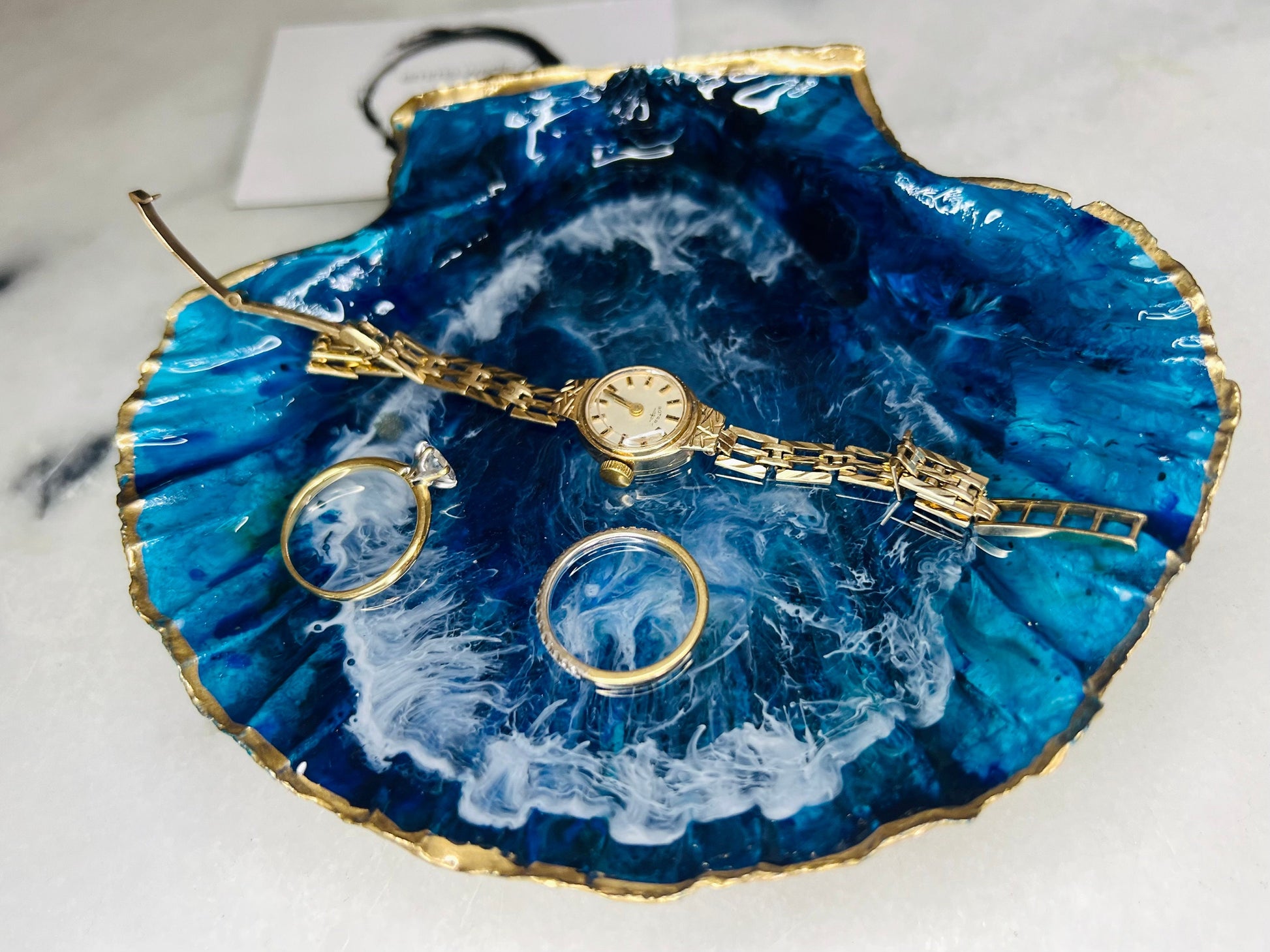Extra large hand painted Dorset scallop shell dish inspired by ocean caves and sea grottos, featuring layered blue acrylic inks and crystal clear resin art with foaming wave details, hand gilded with liquid gold leaf on the rim and reverse, luxury coastal trinket dish, ocean inspired jewellery holder, handmade resin shell decor UK