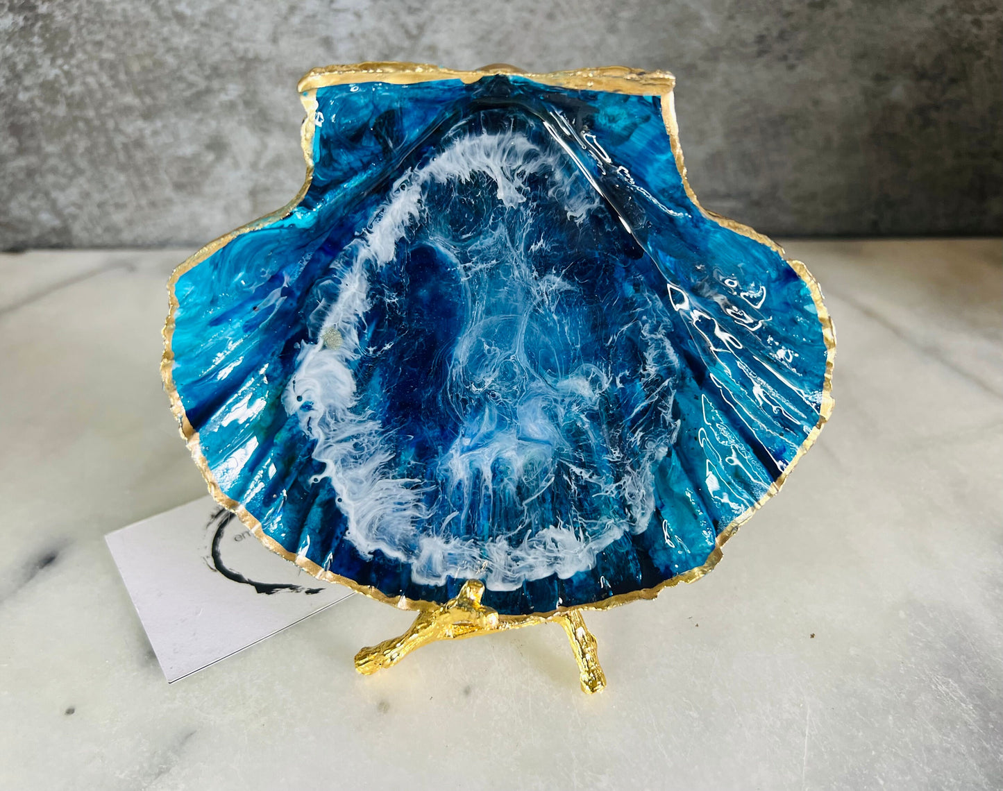 Extra large hand painted Dorset scallop shell dish inspired by ocean caves and sea grottos, featuring layered blue acrylic inks and crystal clear resin art with foaming wave details, hand gilded with liquid gold leaf on the rim and reverse, luxury coastal trinket dish, ocean inspired jewellery holder, handmade resin shell decor UK