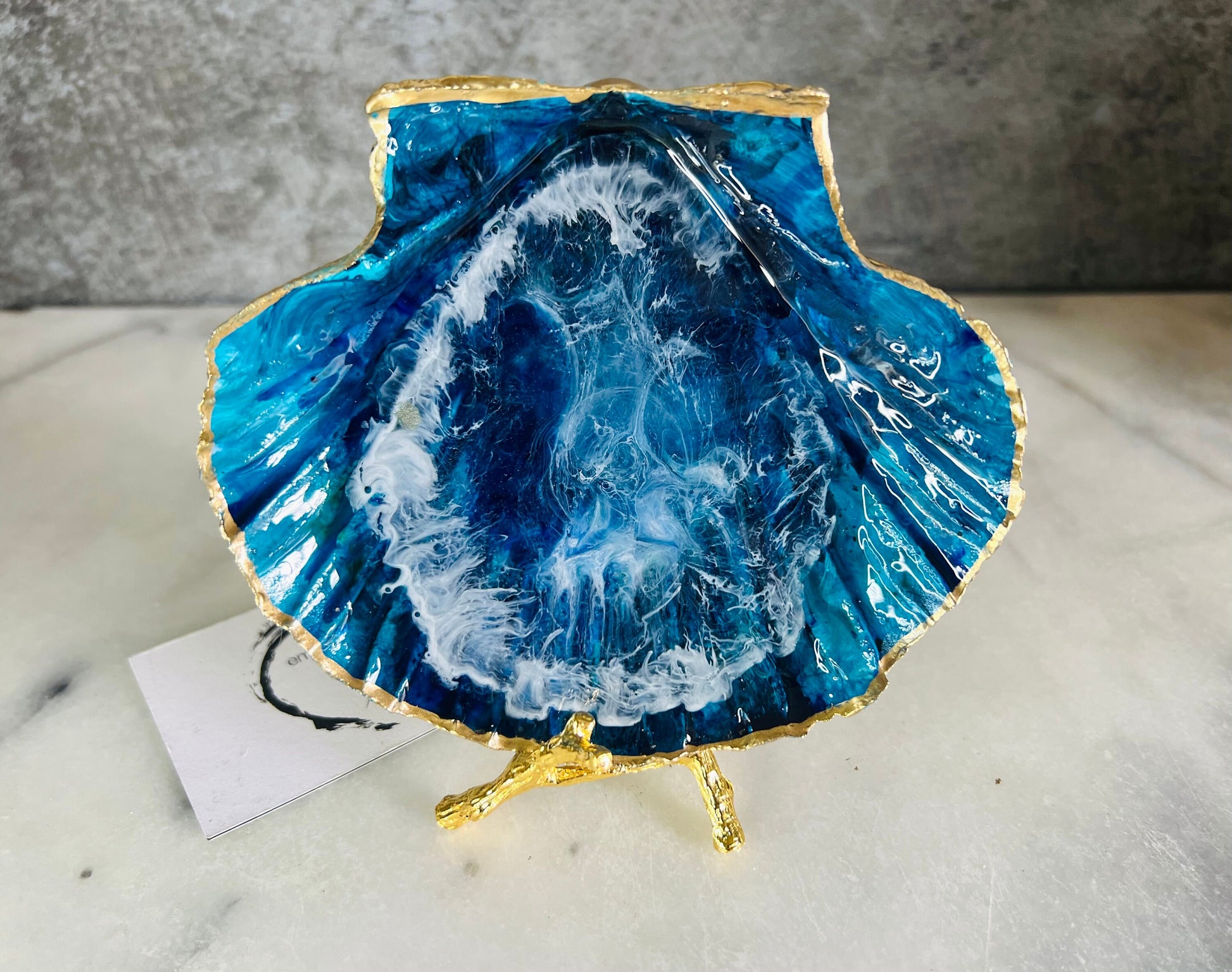 Extra large hand painted Dorset scallop shell dish inspired by ocean caves and sea grottos, featuring layered blue acrylic inks and crystal clear resin art with foaming wave details, hand gilded with liquid gold leaf on the rim and reverse, luxury coastal trinket dish, ocean inspired jewellery holder, handmade resin shell decor UK