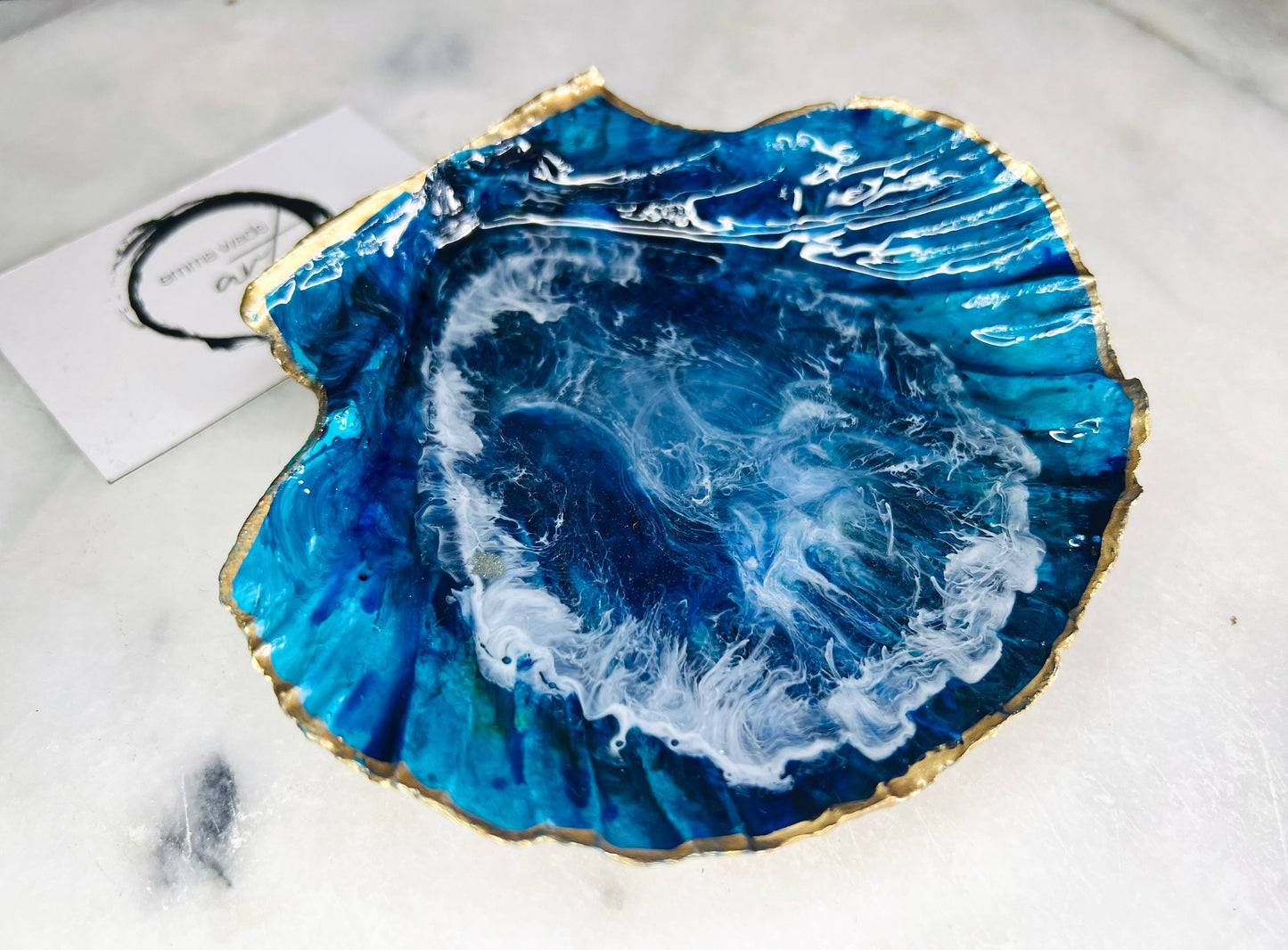Extra large hand painted Dorset scallop shell dish inspired by ocean caves and sea grottos, featuring layered blue acrylic inks and crystal clear resin art with foaming wave details, hand gilded with liquid gold leaf on the rim and reverse, luxury coastal trinket dish, ocean inspired jewellery holder, handmade resin shell decor UK