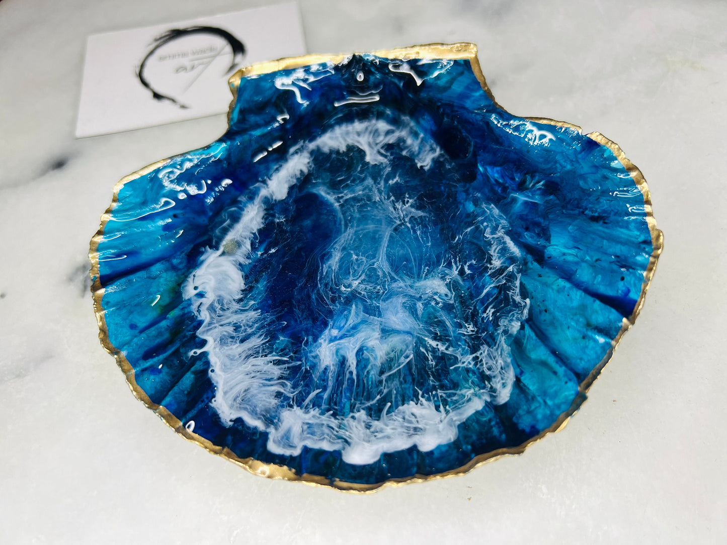 Extra large hand painted Dorset scallop shell dish inspired by ocean caves and sea grottos, featuring layered blue acrylic inks and crystal clear resin art with foaming wave details, hand gilded with liquid gold leaf on the rim and reverse, luxury coastal trinket dish, ocean inspired jewellery holder, handmade resin shell decor UK