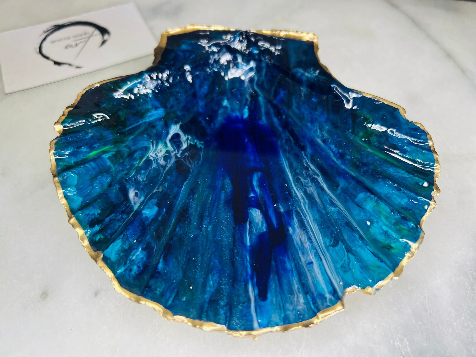 Extra large hand-painted Dorset scallop shell trinket dish featuring deep blue ocean-inspired resin artwork with turquoise wave details, hand gilded gold edging, glossy coastal jewellery holder and luxury seaside décor