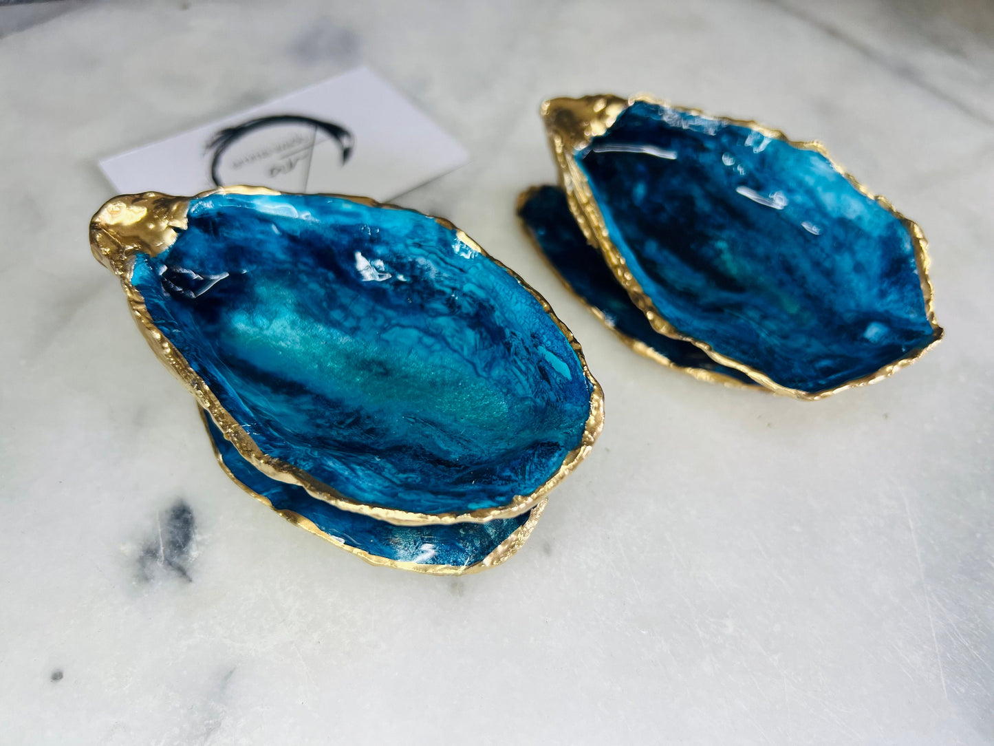 Blue oyster shell ring box, hand painted to resemble ocean waves in rich blue tones with metallic detail and finished with gold leaf edges. Includes a matching painted lid. Each shell is approx. 10cm and crafted from Dorset coastlines, making every piece unique. A stunning ocean-inspired jewellery box, ring bearer box, or proposal ring holder. Perfect for weddings, engagements, anniversaries, or as a keepsake gift for someone special who loves the sea.