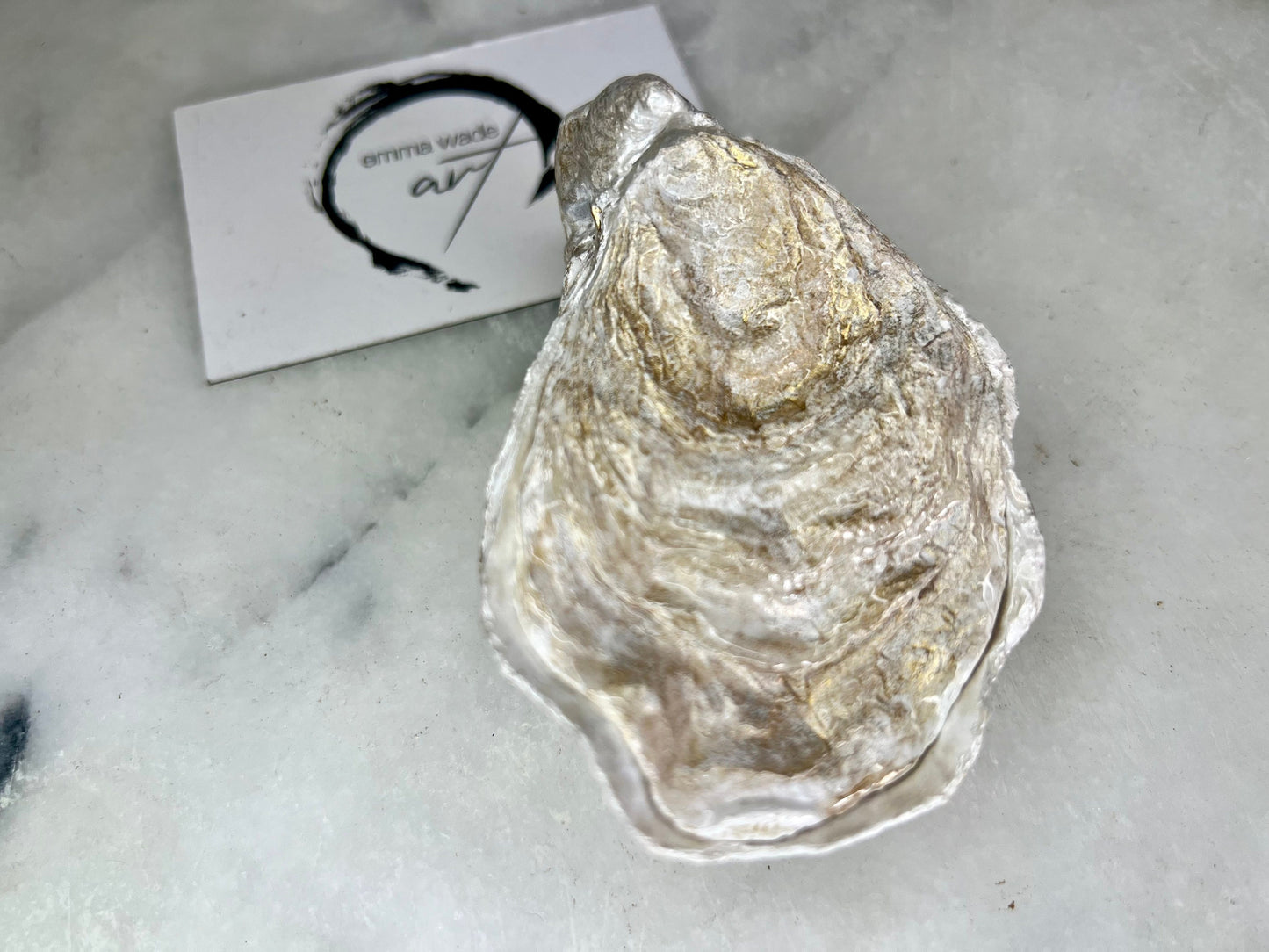 Handcrafted Dorset oyster shell ring box with matching natural shell lid, featuring a luminous inset Swarovski pearl nestled inside the cupped shell. Interior has a soft pearlescent white sheen and is sealed with crystal-clear resin. Optional outer finish in natural pearl tone or pearl with subtle gold leaf highlights. Coastal-inspired engagement proposal ring holder and wedding keepsake, styled on marble surface.