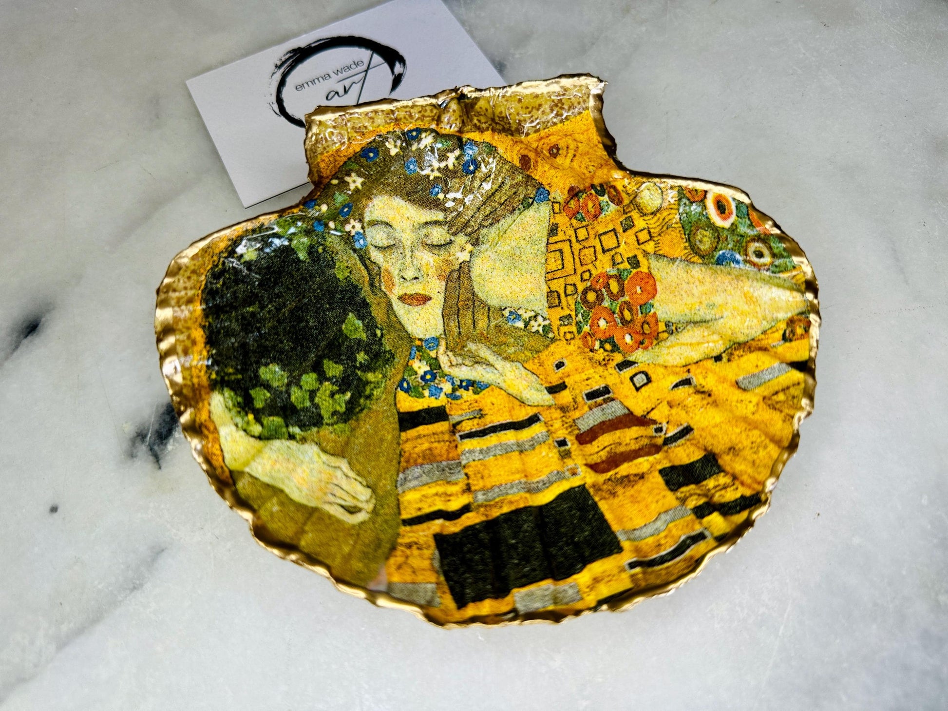 Handmade scallop shell trinket dish inspired by Gustav Klimt’s “The Kiss”, finished with gold leaf and sealed with glossy resin. Coastal Dorset shell jewellery dish perfect for rings, earrings and small treasures. Unique decorative shell bowl with golden artwork design, photographed on a light background showing detailed gilded surface and natural shell shape.
