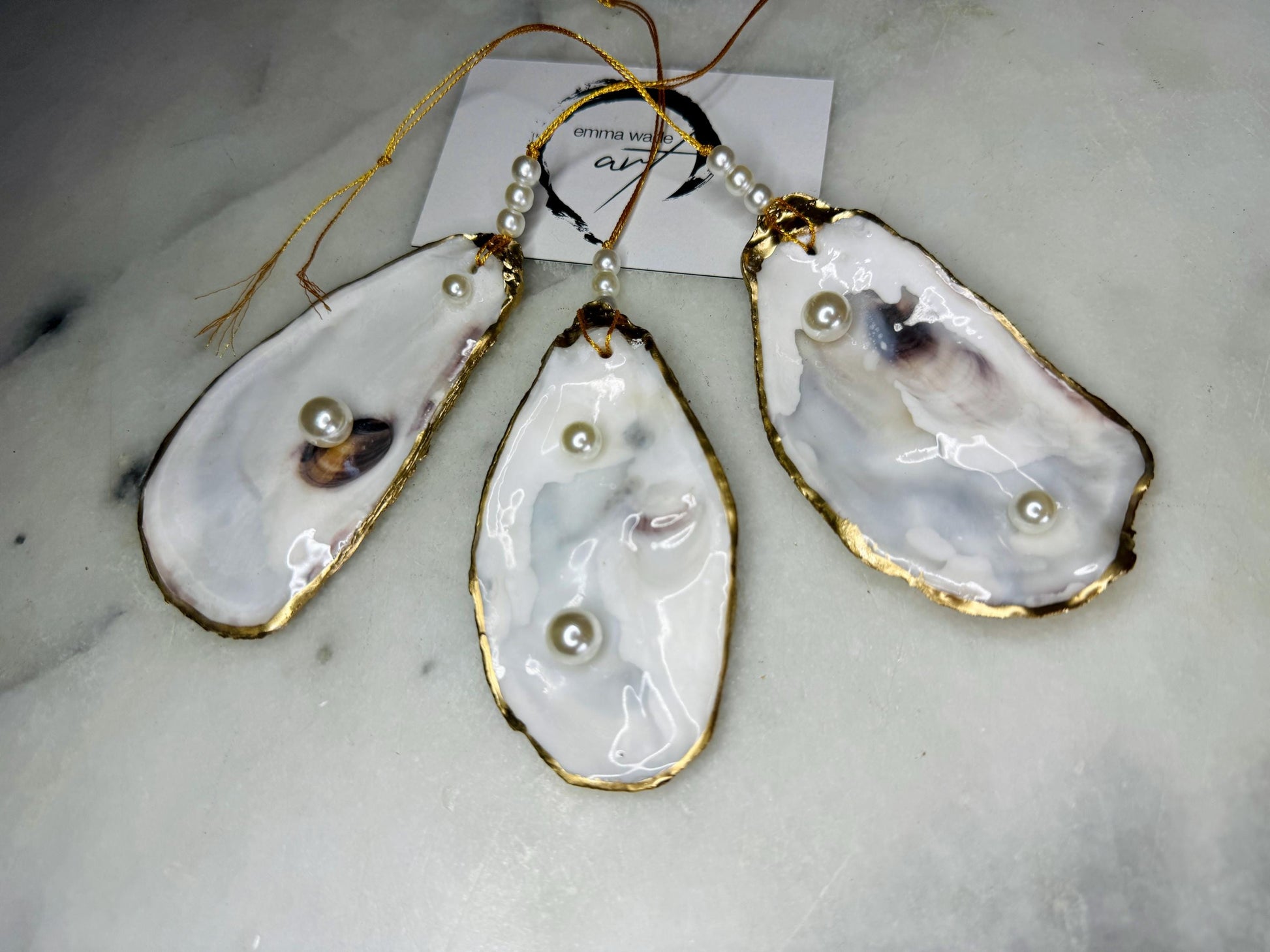 Luxury flat pearl oyster shell hanging ornaments handcrafted from natural Dorset oyster shells with glossy pearlescent interiors, two Swarovski pearls per ornament and hand-painted gold leaf edging. Elegant coastal hanging decor finished in crystal clear resin with gold hanging cord and pearl bead details. Available individually or as a set of three. Perfect for beach house interiors, luxury bathroom styling, wedding gifts, coastal Christmas decor and year-round shell home decor.