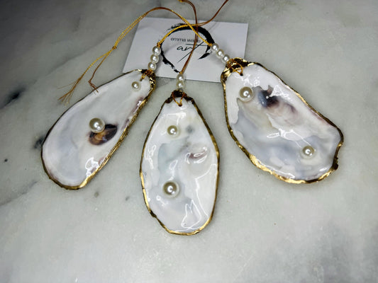 Luxury flat pearl oyster shell hanging ornaments handcrafted from natural Dorset oyster shells with glossy pearlescent interiors, two Swarovski pearls per ornament and hand-painted gold leaf edging. Elegant coastal hanging decor finished in crystal clear resin with gold hanging cord and pearl bead details. Available individually or as a set of three. Perfect for beach house interiors, luxury bathroom styling, wedding gifts, coastal Christmas decor and year-round shell home decor.