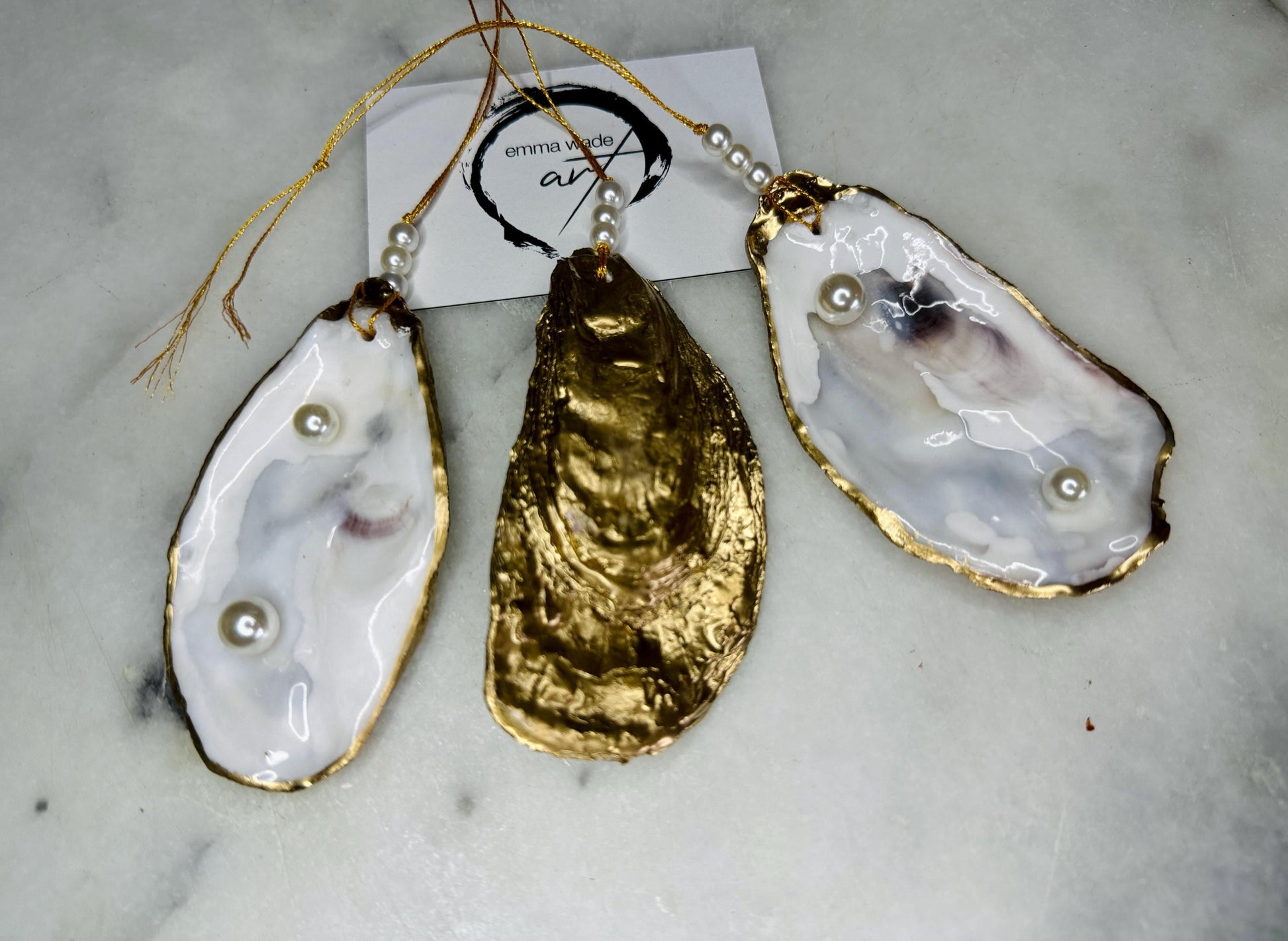 Luxury flat pearl oyster shell hanging ornaments handcrafted from natural Dorset oyster shells with glossy pearlescent interiors, two Swarovski pearls per ornament and hand-painted gold leaf edging. Elegant coastal hanging decor finished in crystal clear resin with gold hanging cord and pearl bead details. Available individually or as a set of three. Perfect for beach house interiors, luxury bathroom styling, wedding gifts, coastal Christmas decor and year-round shell home decor.