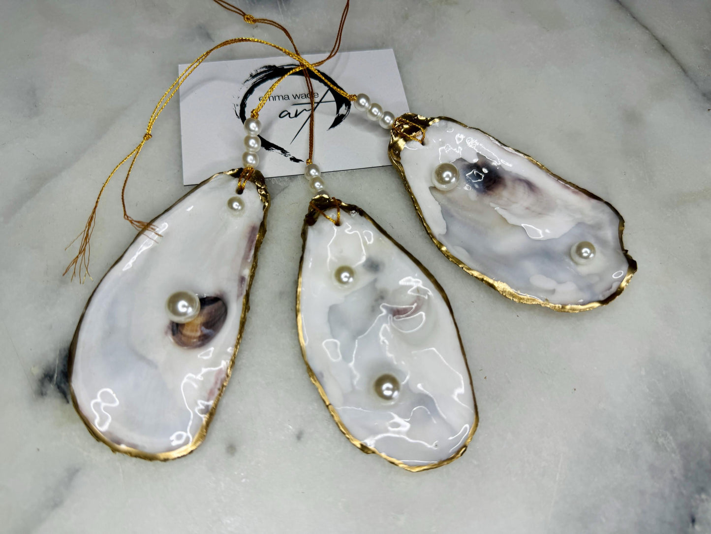 Luxury flat pearl oyster shell hanging ornaments handcrafted from natural Dorset oyster shells with glossy pearlescent interiors, two Swarovski pearls per ornament and hand-painted gold leaf edging. Elegant coastal hanging decor finished in crystal clear resin with gold hanging cord and pearl bead details. Available individually or as a set of three. Perfect for beach house interiors, luxury bathroom styling, wedding gifts, coastal Christmas decor and year-round shell home decor.