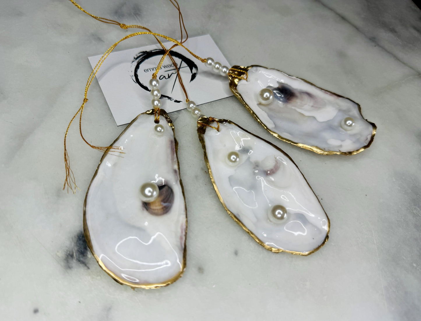 Luxury flat pearl oyster shell hanging ornaments handcrafted from natural Dorset oyster shells with glossy pearlescent interiors, two Swarovski pearls per ornament and hand-painted gold leaf edging. Elegant coastal hanging decor finished in crystal clear resin with gold hanging cord and pearl bead details. Available individually or as a set of three. Perfect for beach house interiors, luxury bathroom styling, wedding gifts, coastal Christmas decor and year-round shell home decor.