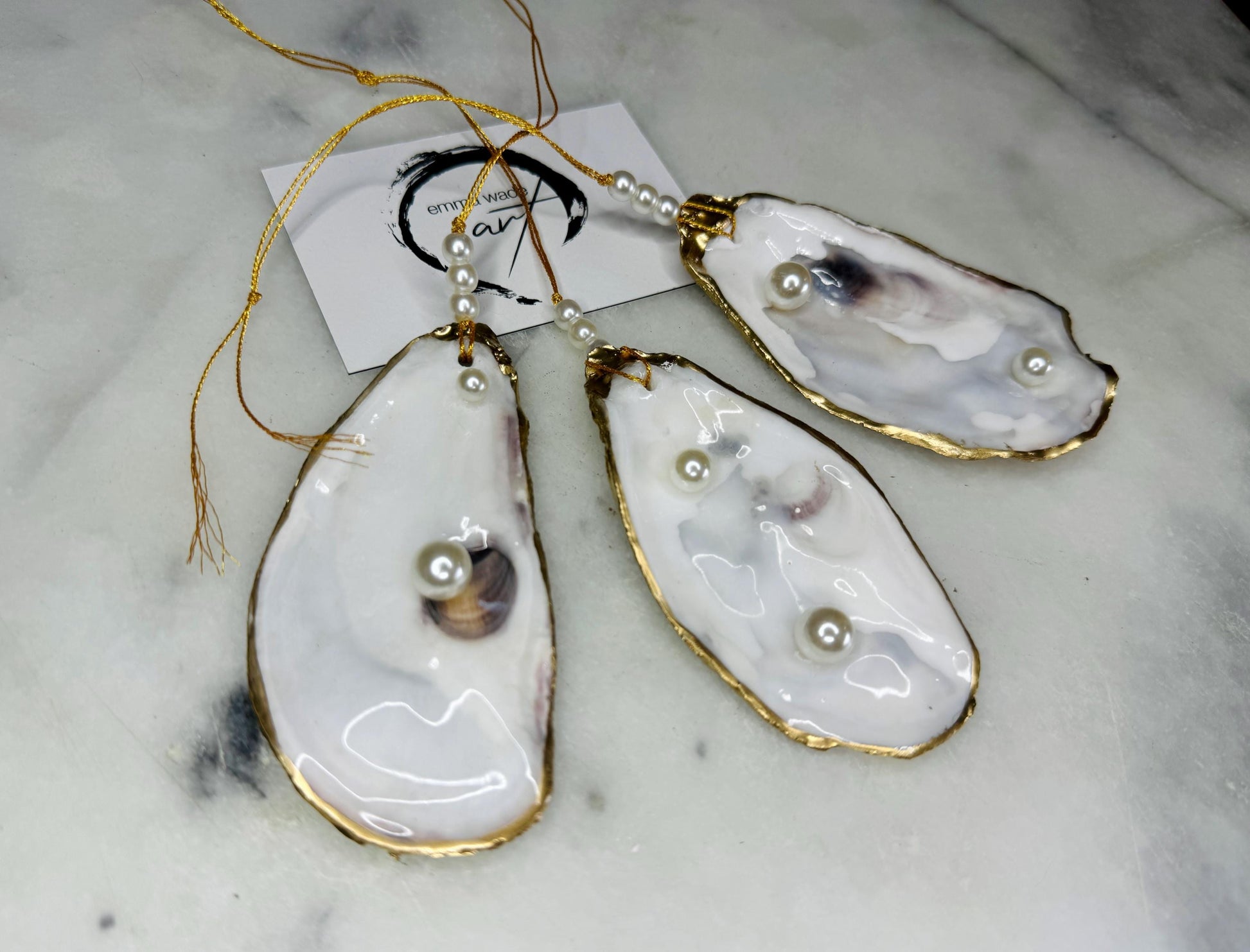 Luxury flat pearl oyster shell hanging ornaments handcrafted from natural Dorset oyster shells with glossy pearlescent interiors, two Swarovski pearls per ornament and hand-painted gold leaf edging. Elegant coastal hanging decor finished in crystal clear resin with gold hanging cord and pearl bead details. Available individually or as a set of three. Perfect for beach house interiors, luxury bathroom styling, wedding gifts, coastal Christmas decor and year-round shell home decor.
