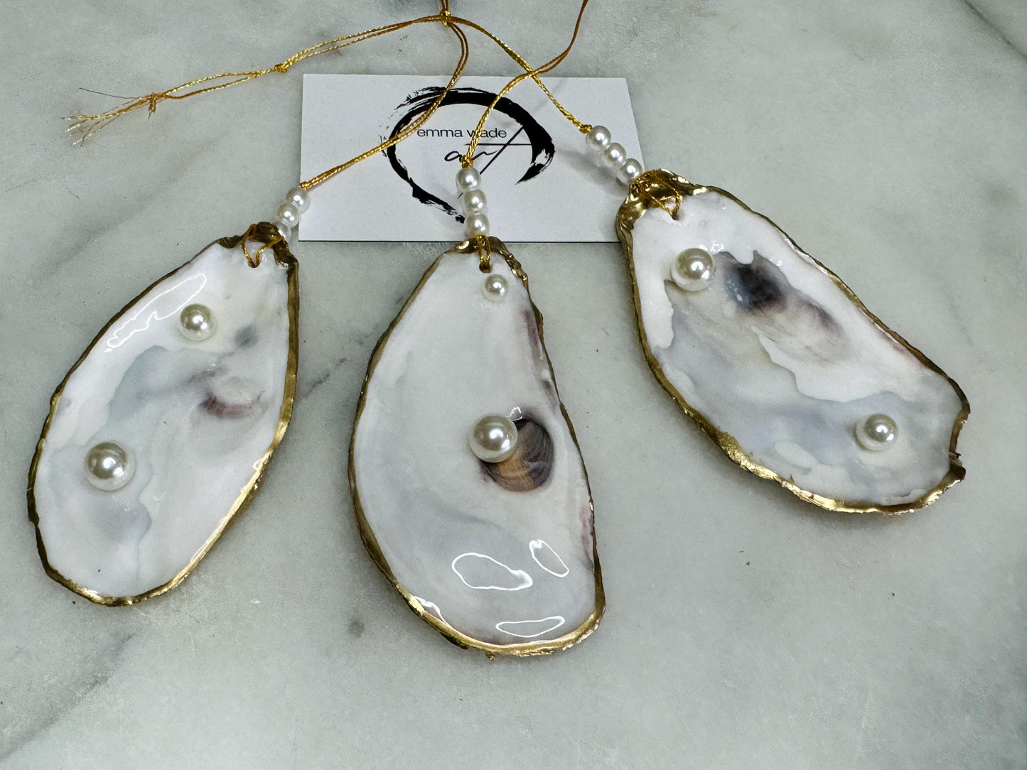 Luxury flat pearl oyster shell hanging ornaments handcrafted from natural Dorset oyster shells with glossy pearlescent interiors, two Swarovski pearls per ornament and hand-painted gold leaf edging. Elegant coastal hanging decor finished in crystal clear resin with gold hanging cord and pearl bead details. Available individually or as a set of three. Perfect for beach house interiors, luxury bathroom styling, wedding gifts, coastal Christmas decor and year-round shell home decor.